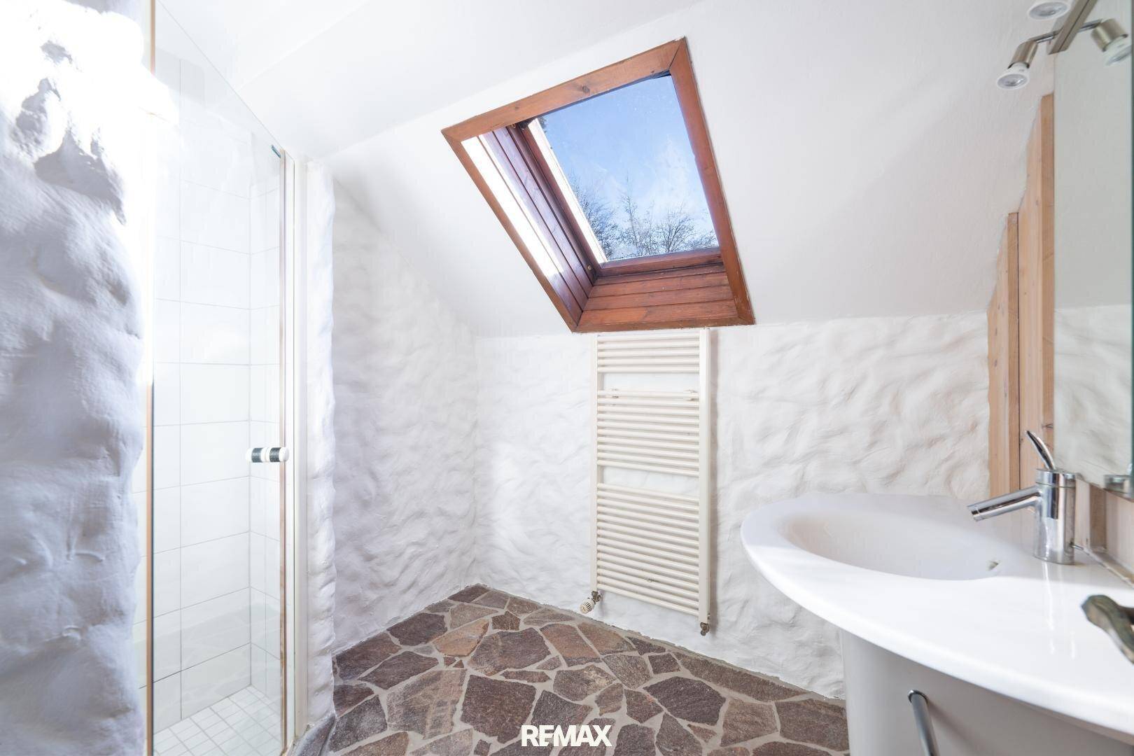 Modernes Badezimmer im Dachgeschoss mit Dusche, Dachfenster und Steinboden.