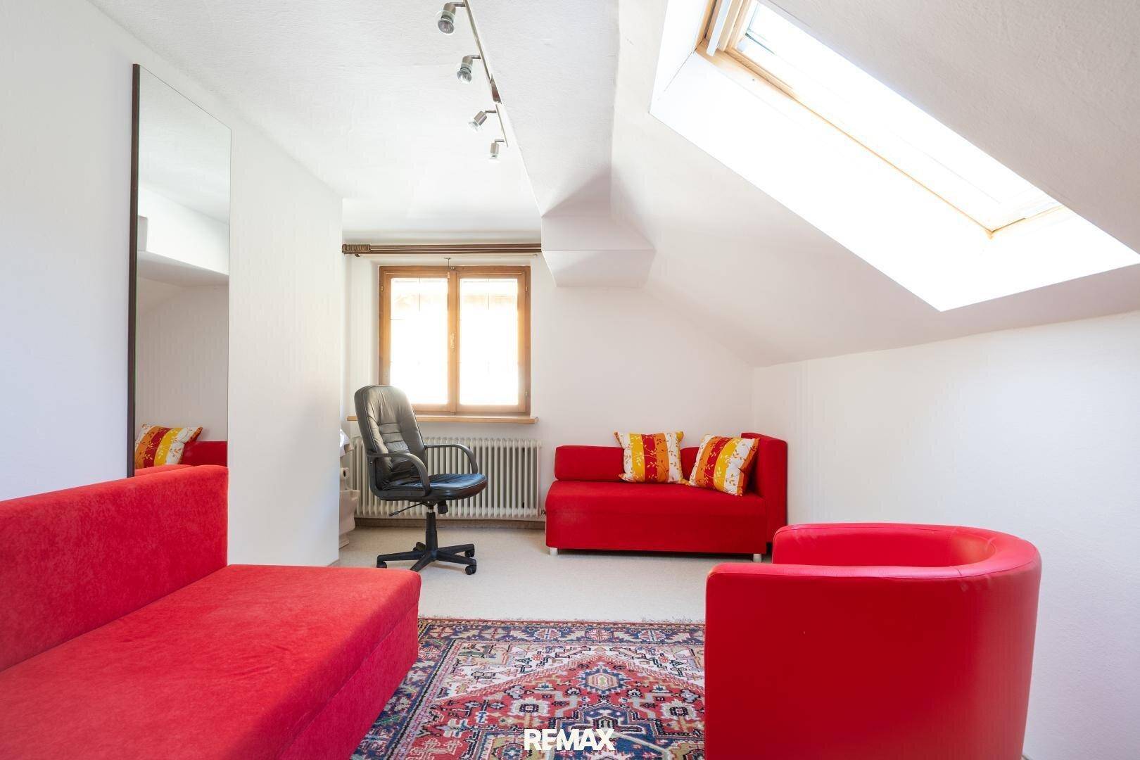 Helles Dachzimmer mit roten Möbeln, Teppichboden und Dachfenster.