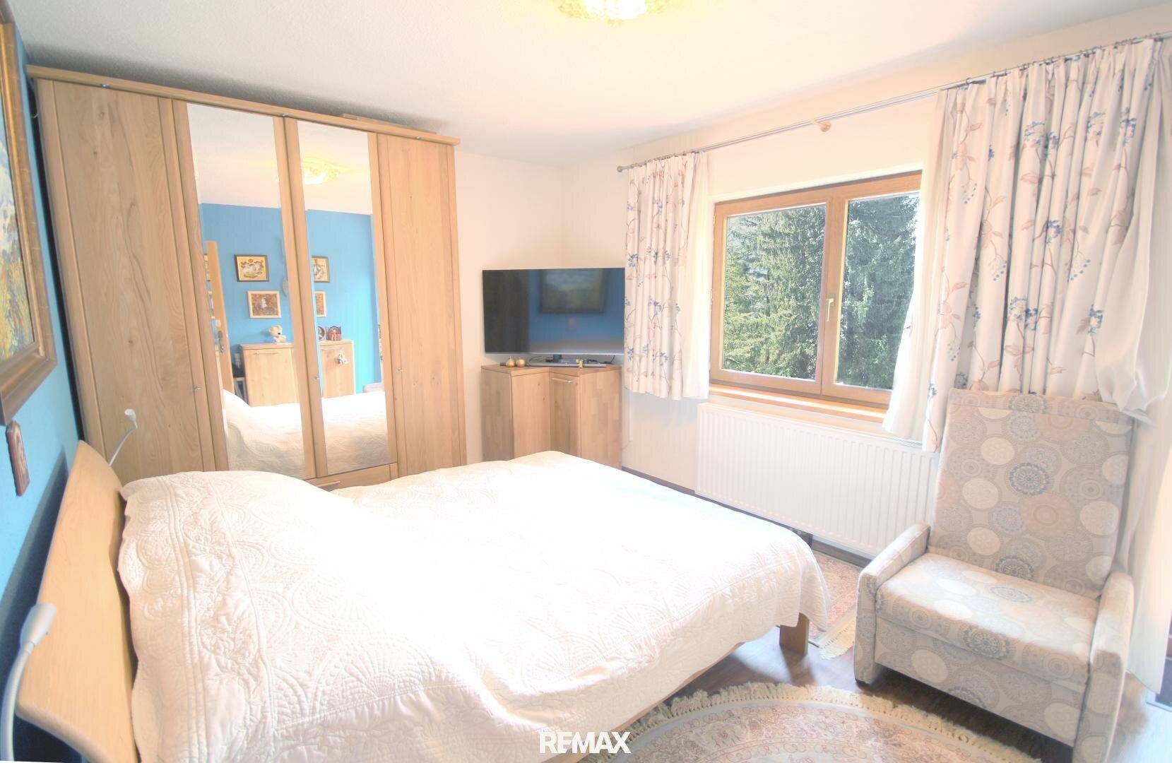 Geräumiges Schlafzimmer mit Doppelbett, Spiegelschrank und Fenster mit Blick ins Grüne.