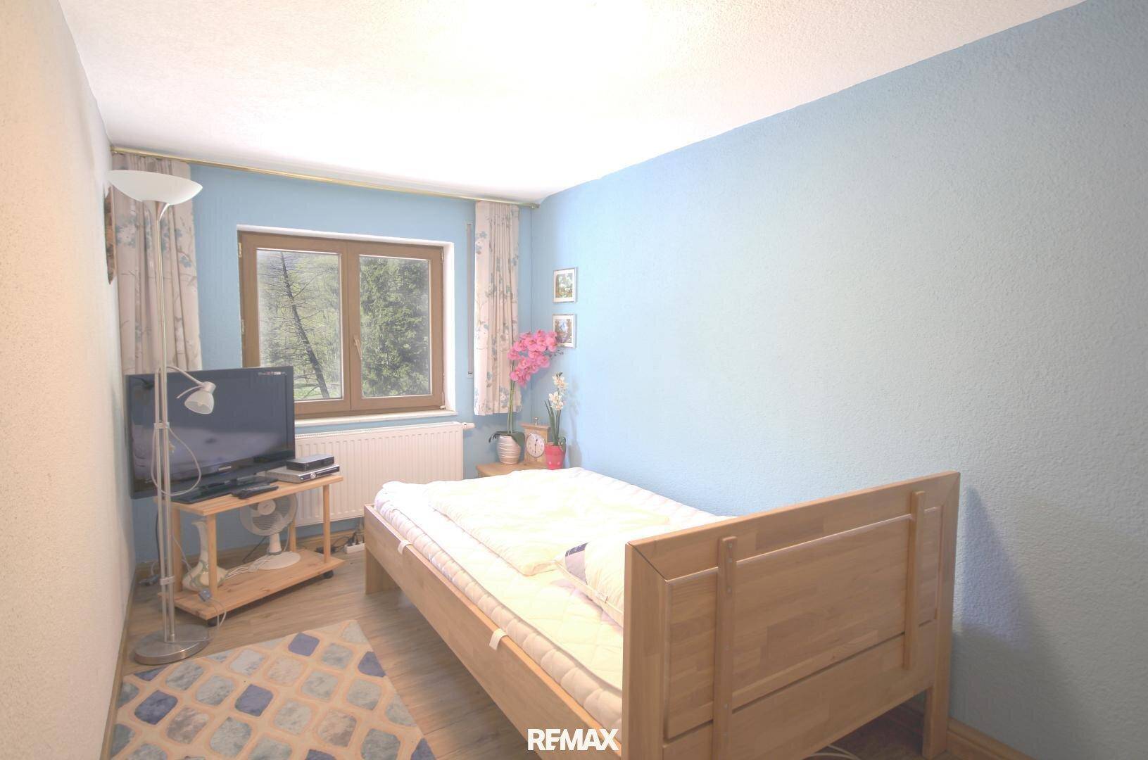 Kleines Schlafzimmer mit Einzelbett, blauen Wänden und Fenster mit Blick ins Grüne.