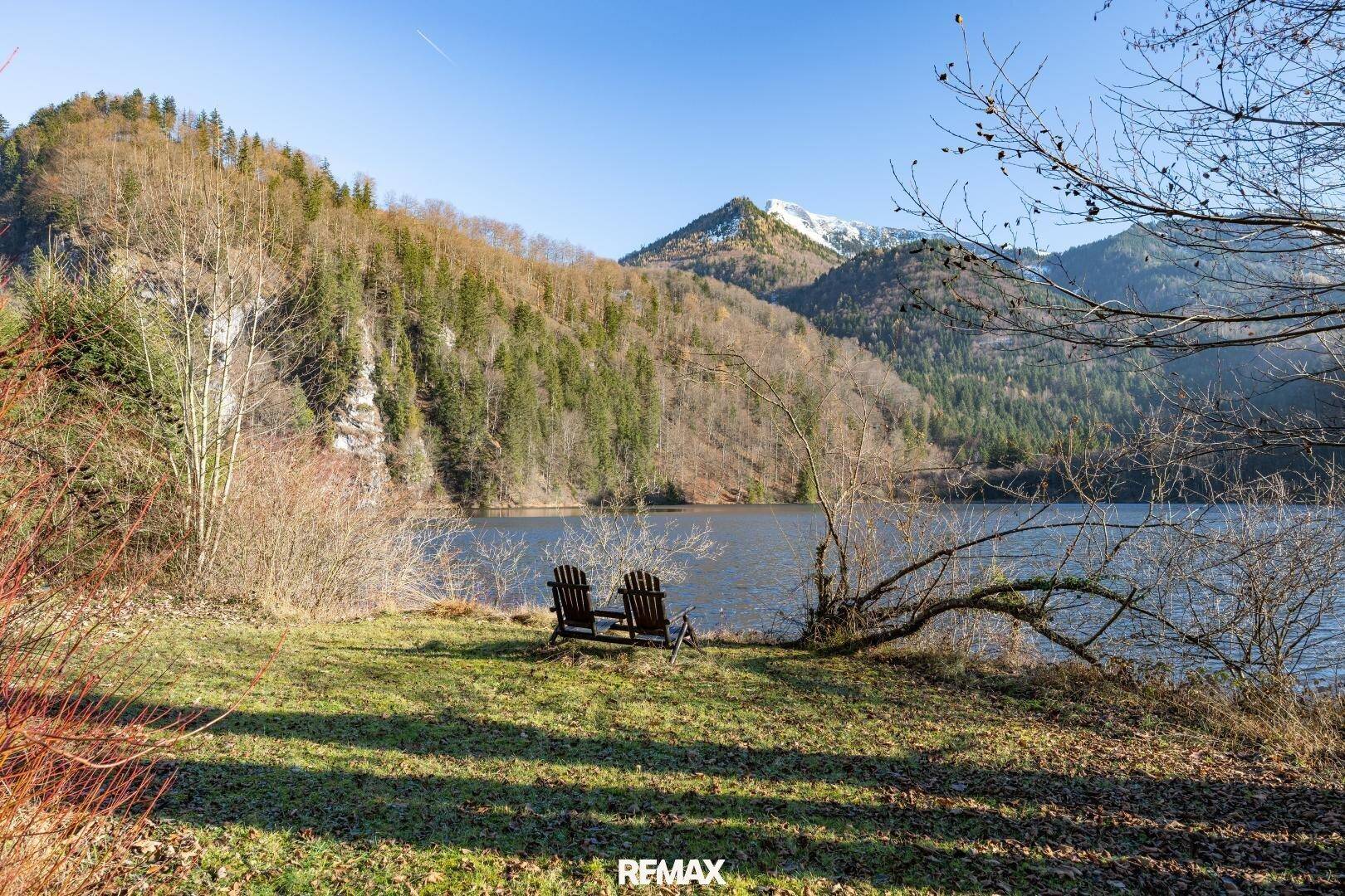 Malerischer Blick auf den See und die umliegenden Berge mit zwei Stühlen am Ufer.