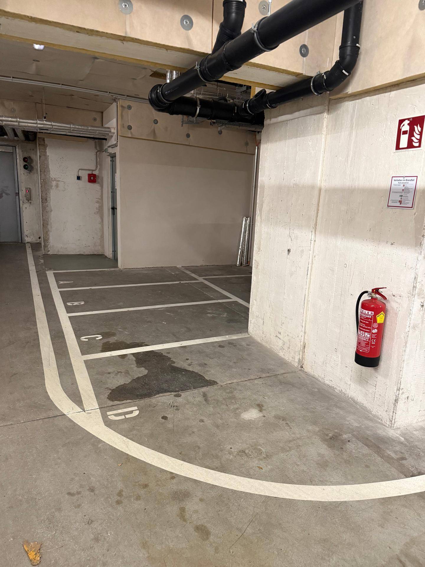 Ecke einer Tiefgarage mit markierten Stellplätzen, Betonwänden und einem Feuerlöscher.