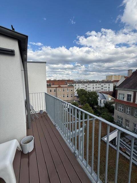 Balkon mit Holzdielen und Metallgeländer, bietet einen weiten Blick über begrünte Dächer und die Stadt.