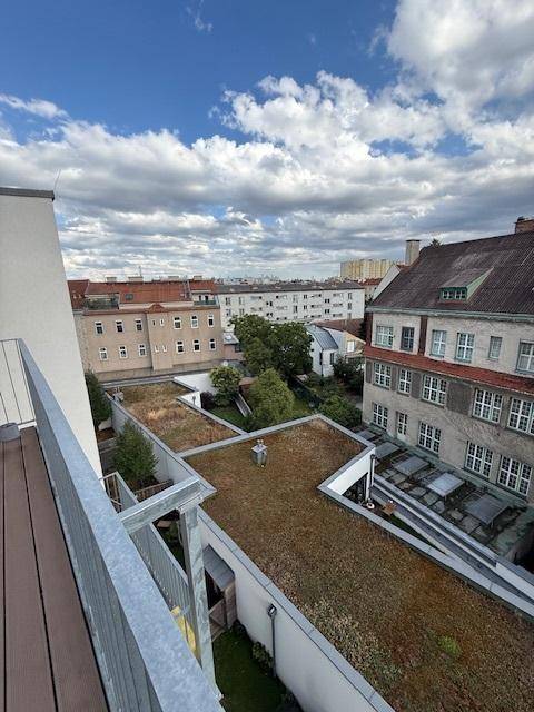 Blick von einem Balkon auf begrünte Dächer und die umliegende Stadtlandschaft unter bewölktem Himmel.