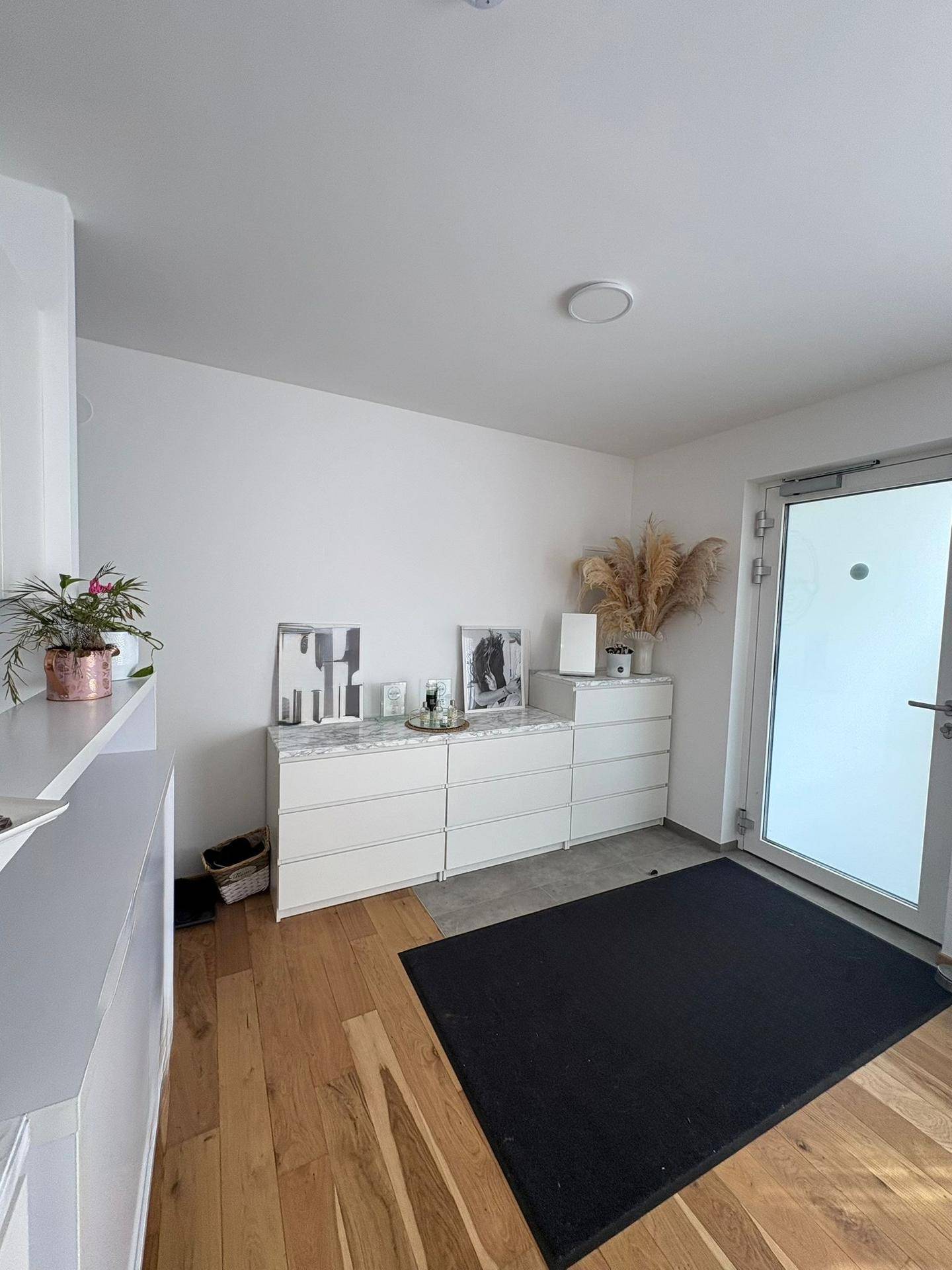 Heller Eingangsbereich mit Holzboden, weißer Kommode und moderner Dekoration.