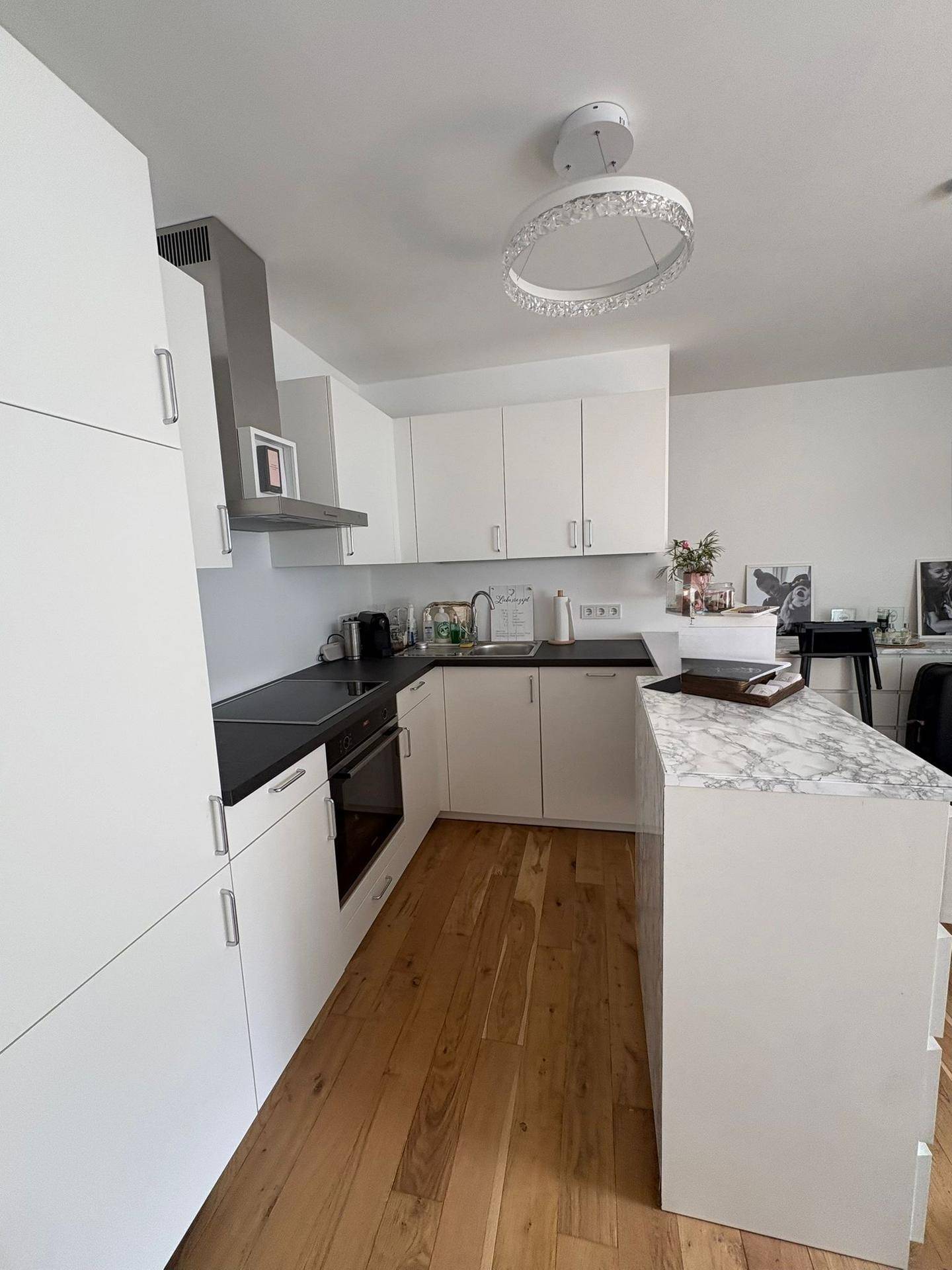 Moderne weiße Küche mit Holzboden, Einbaugeräten und einer Kochinsel mit Marmorplatte.