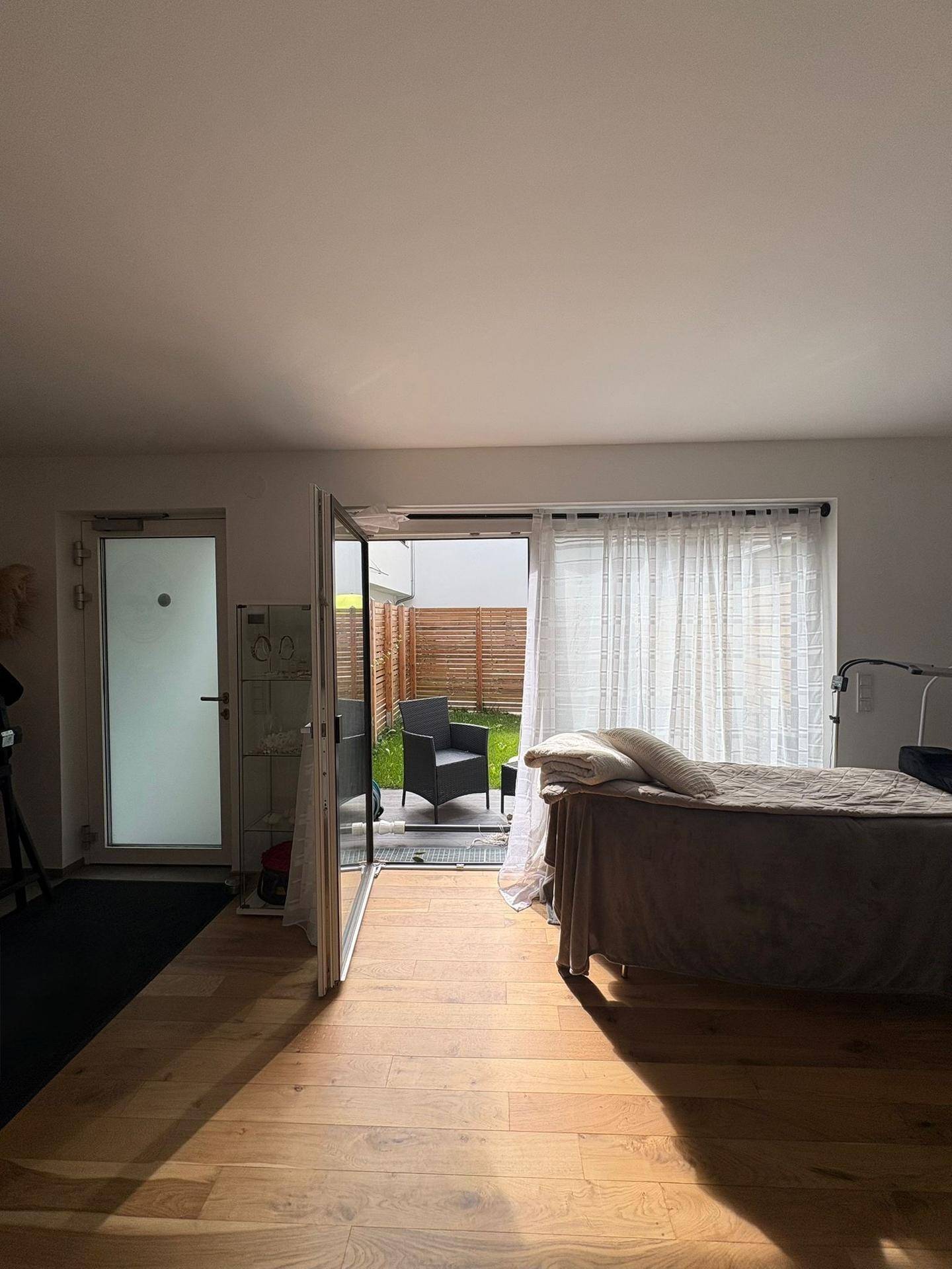 Helles Zimmer mit Holzboden und großen Glastüren, die Zugang zum Gartenbereich bieten.