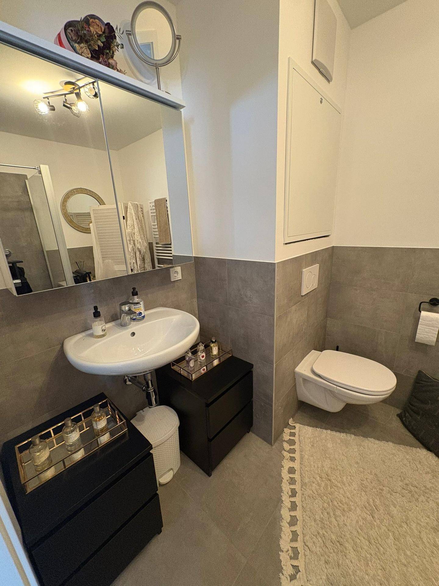 Modernes Badezimmer mit grauen Fliesen, wandhängendem WC und Waschbecken mit Spiegelschrank.