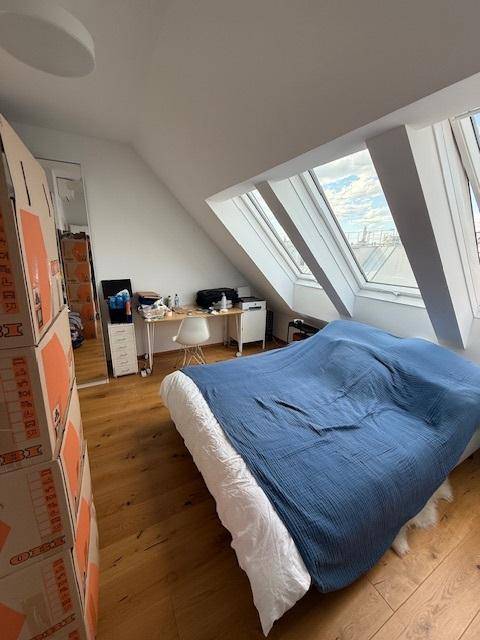 Helles Schlafzimmer im Dachgeschoss mit Holzboden, schrägen Wänden und großen Dachfenstern.