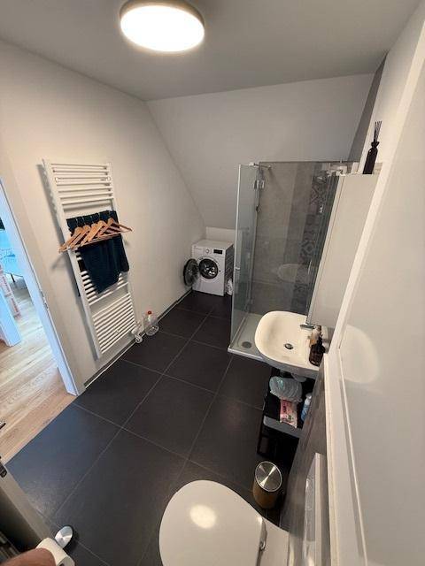 Modernes Badezimmer mit dunklen Fliesen, Duschkabine, Waschmaschine und beheiztem Handtuchhalter.