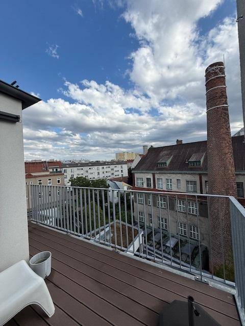 Geräumiger Balkon mit Holzdielen und Metallgeländer, bietet einen Blick auf einen Schornstein und die Stadt.