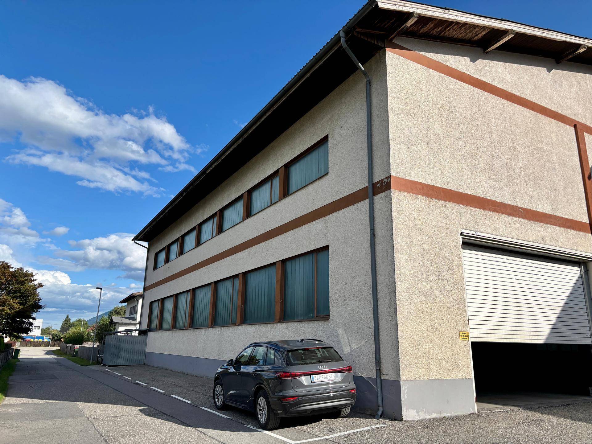 Außenansicht des Industriegebäudes mit Rolltor, mehreren Fenstern und geparktem Auto.