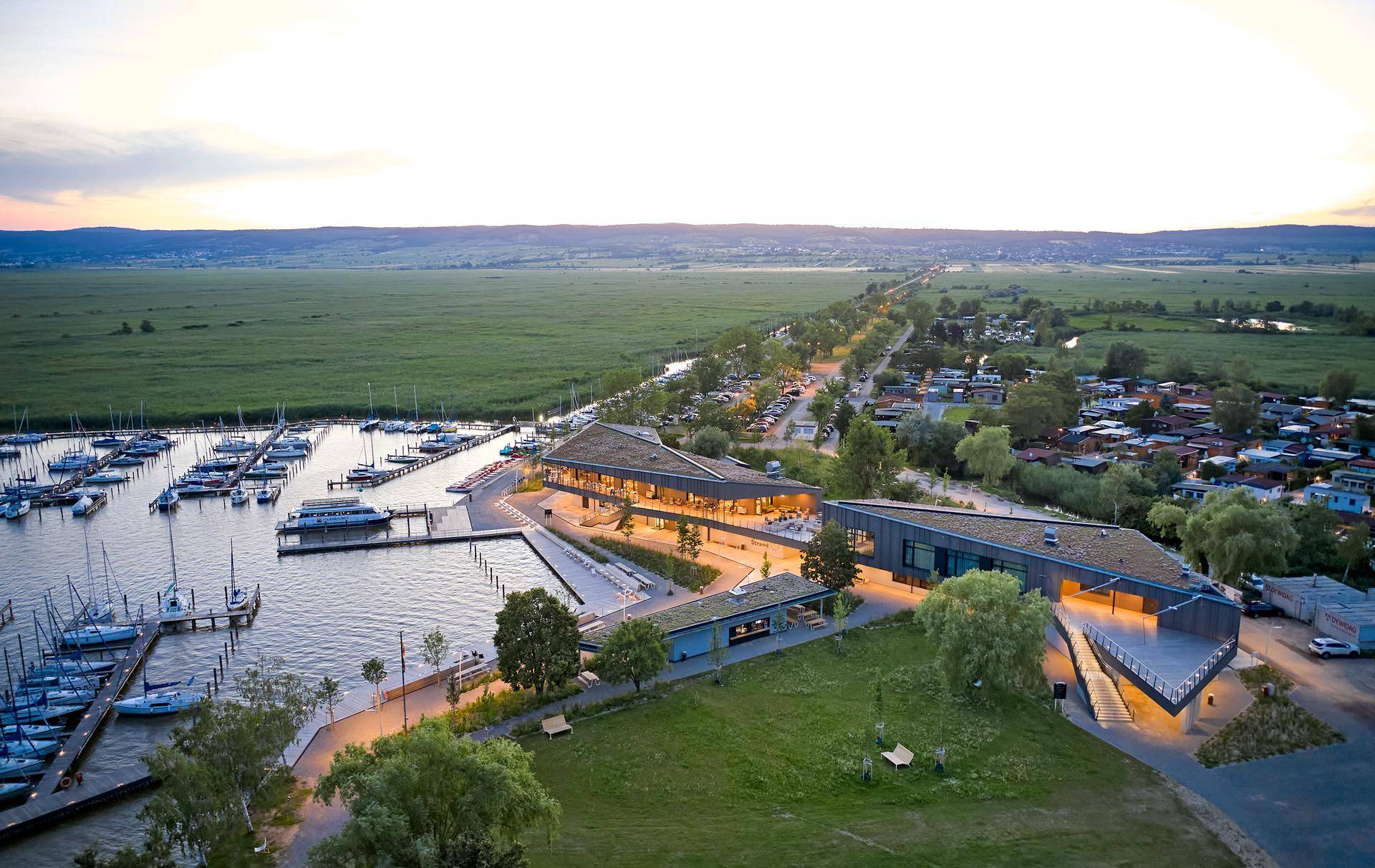 Abendliche Luftaufnahme eines modernen Yachthafens mit Gebäuden und weitem Blick über die Landschaft.
