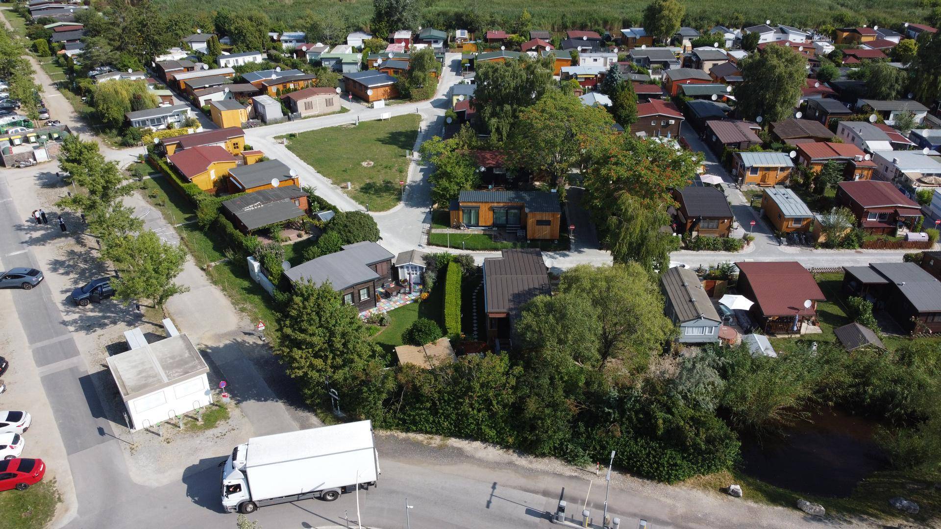 Luftaufnahme einer Siedlung mit vielen kleinen Häusern und viel Grün, umgeben von Straßen und Bäumen.