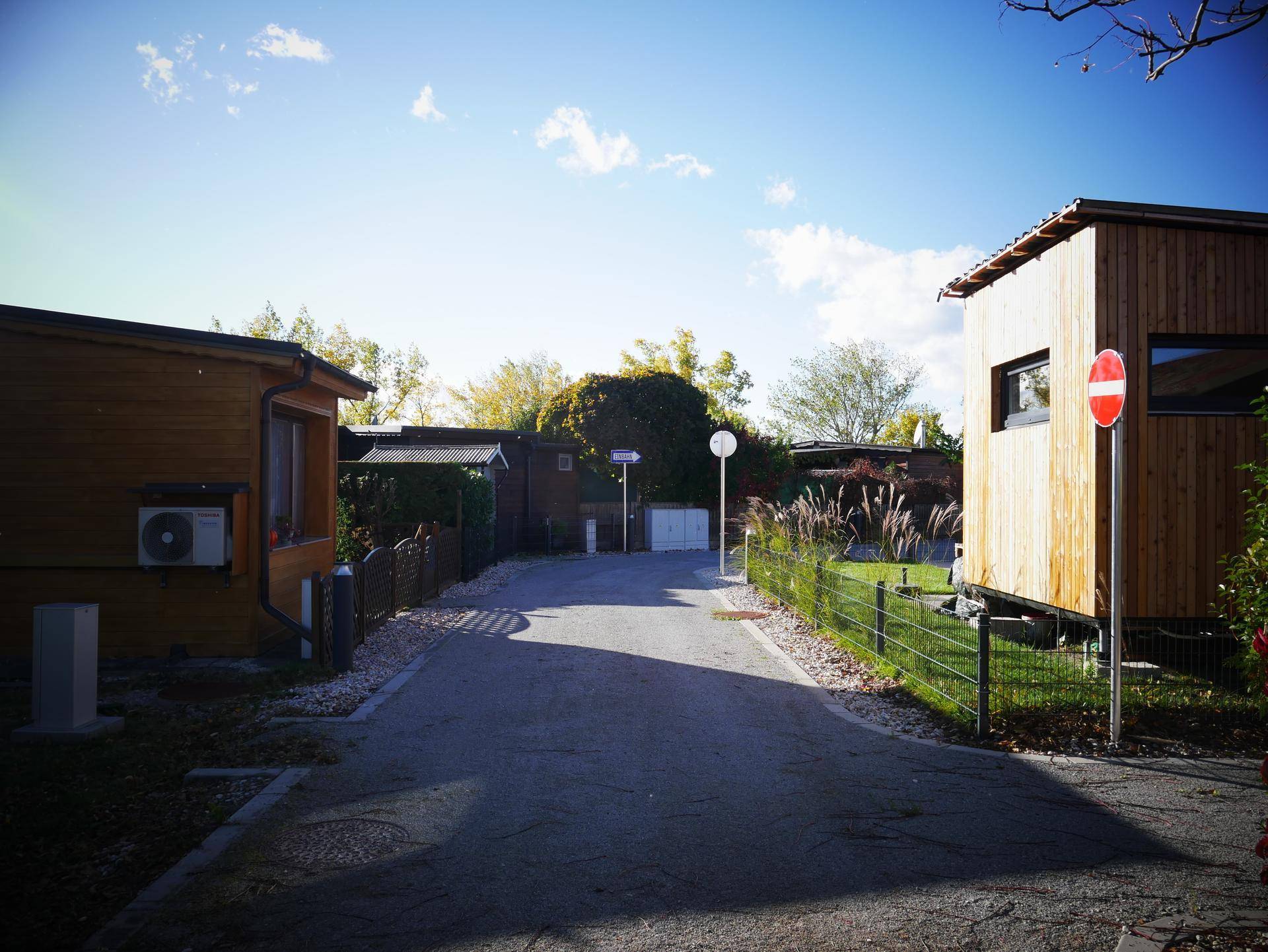 Sonnige Straße in einer Siedlung mit modernen Holzhäusern und gepflegten Gärten.