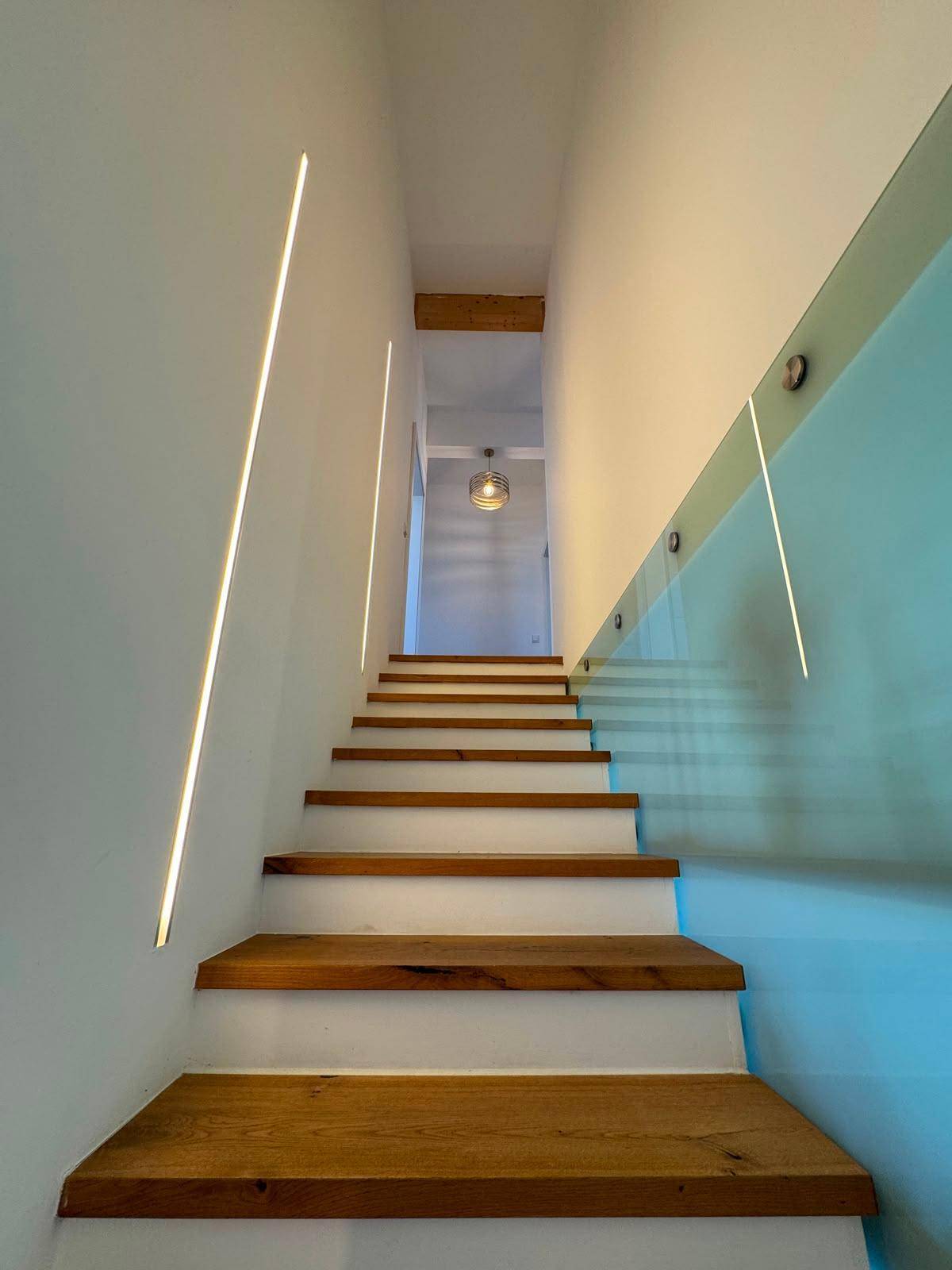 Moderne Holztreppe mit Glasgeländer und integrierter LED-Beleuchtung.