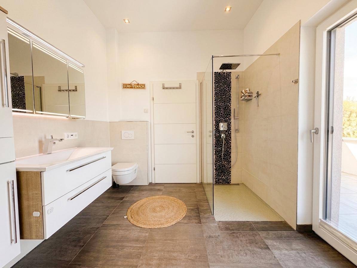 Modernes Badezimmer mit ebenerdiger Dusche, Doppelwaschbecken und Zugang zu einem Außenbereich.