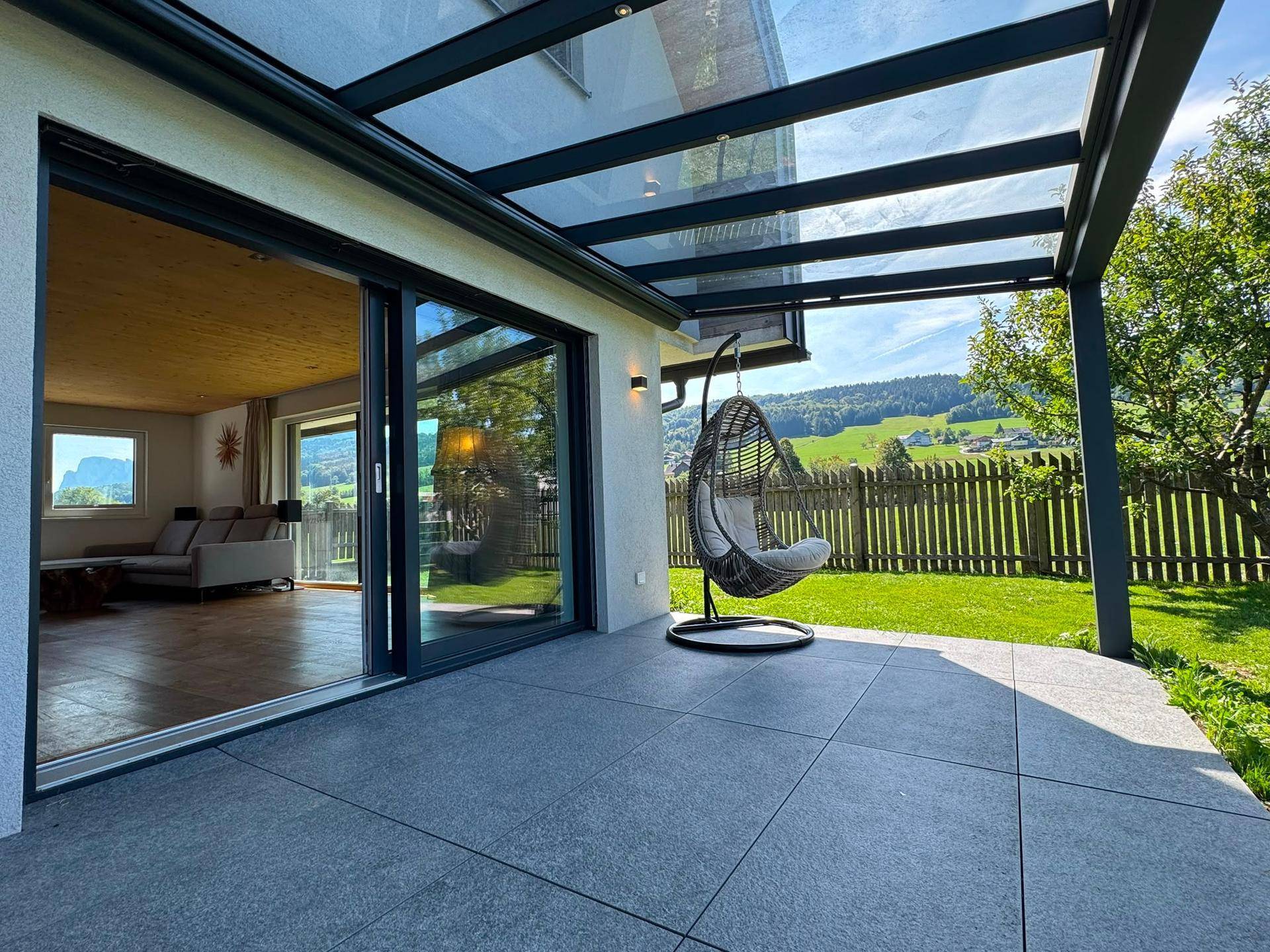 Überdachte Terrasse mit Hängesessel, Rasenzugang und weitem Blick ins Grüne.