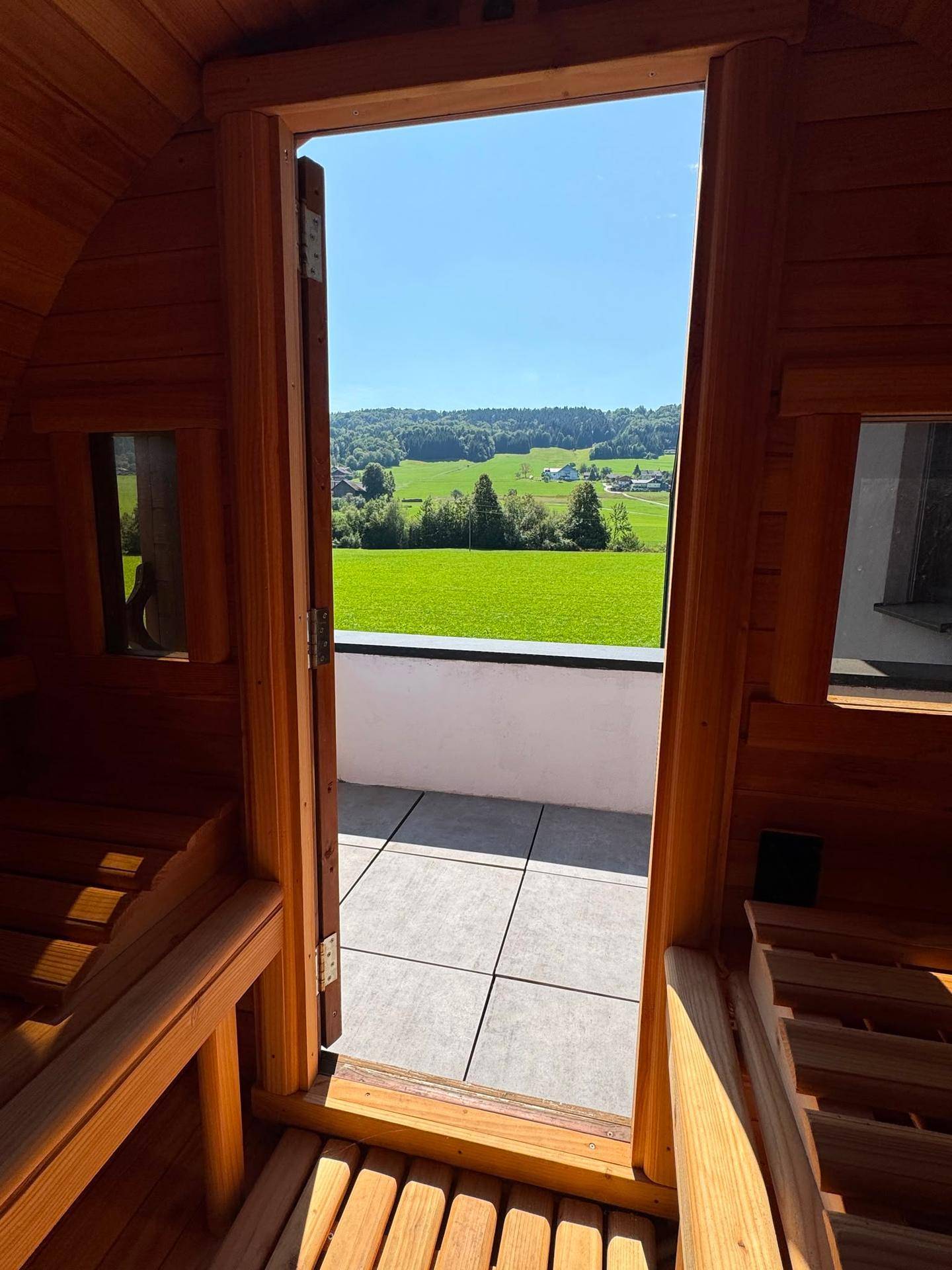 Innenansicht einer Fasssauna mit Blick auf die Terrasse und die umliegende Natur.