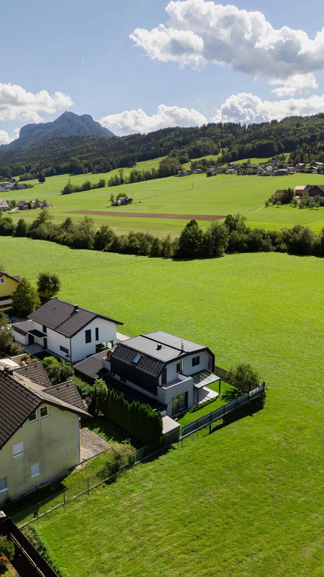 Weitläufige grüne Landschaft mit Bergen und einem modernen Wohnhaus in ländlicher Umgebung.