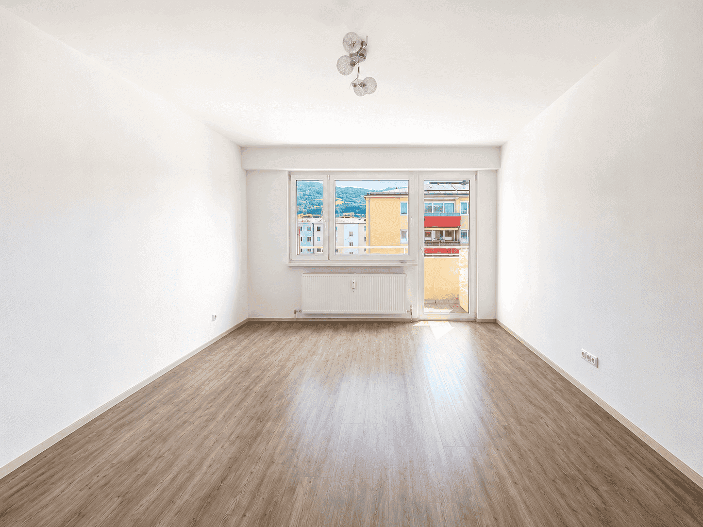 Heller Raum mit Laminatboden und Zugang zu einem kleinen Balkon mit Stadtblick.