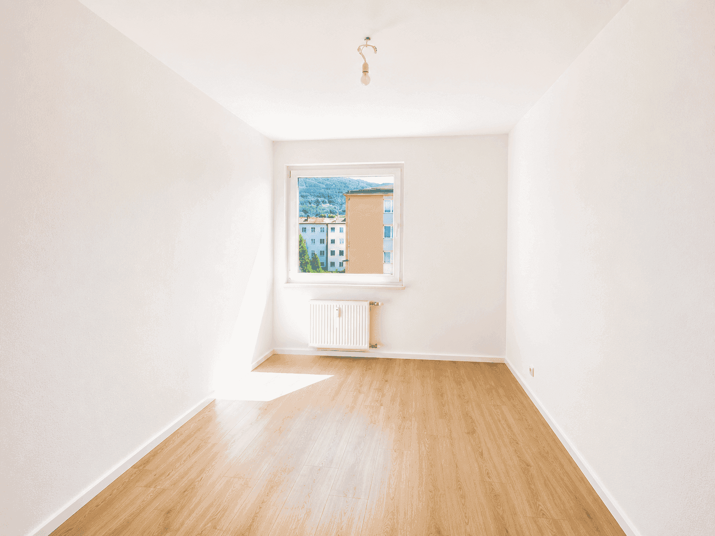 Helles, leeres Zimmer mit Laminatboden und Fensterblick ins Grüne, bereit zur individuellen Gestaltung.