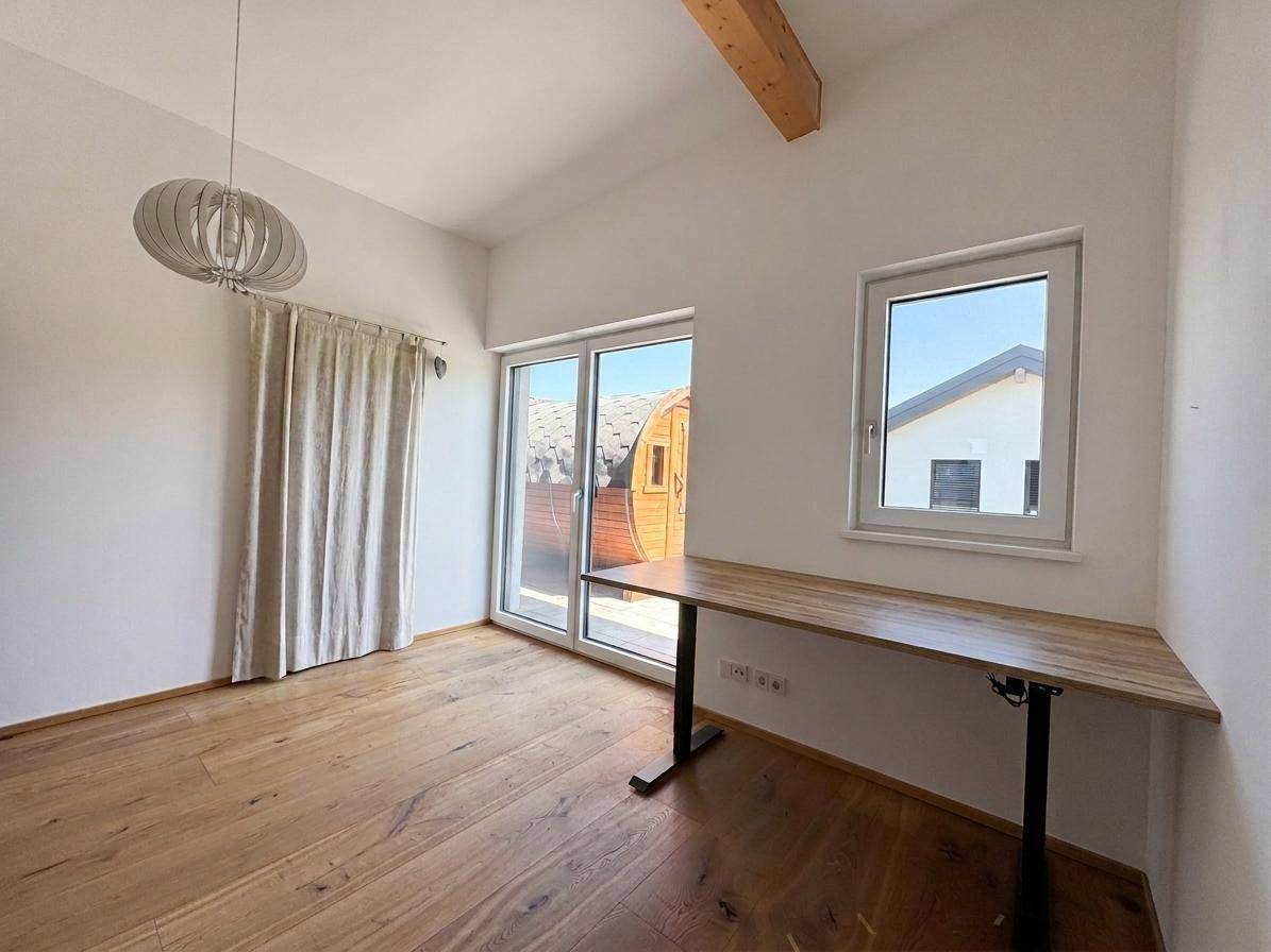 Heller Raum mit Holzboden, Schreibtisch und Zugang zu einer Terrasse mit Fasssauna.