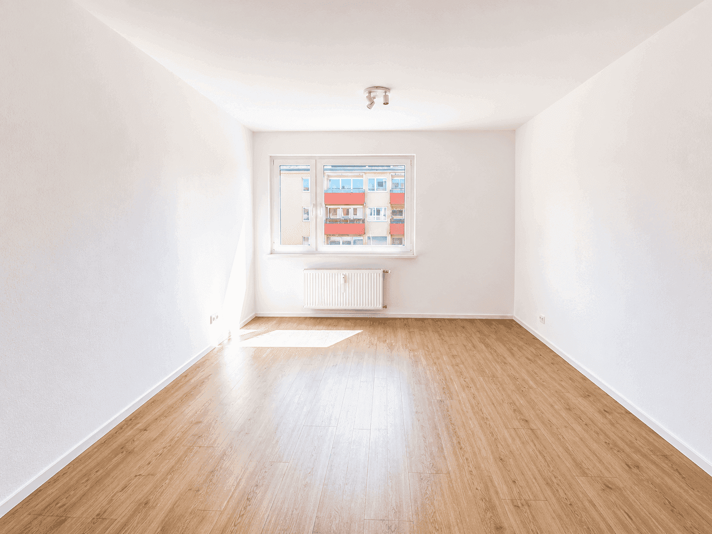 Heller, leerer Raum mit Holzfußboden und großem Fenster, ideal als Wohnzimmer.