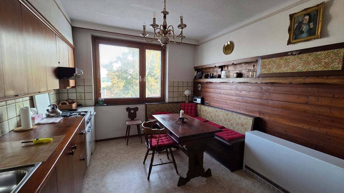 Traditionelle Küche mit Holzelementen, Essecke und Fenster mit natürlichem Lichteinfall.