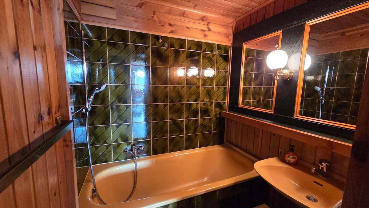 Badezimmer im 80er-Jahre-Stil mit grünen Fliesen, Holzverkleidung und gelber Badewanne.