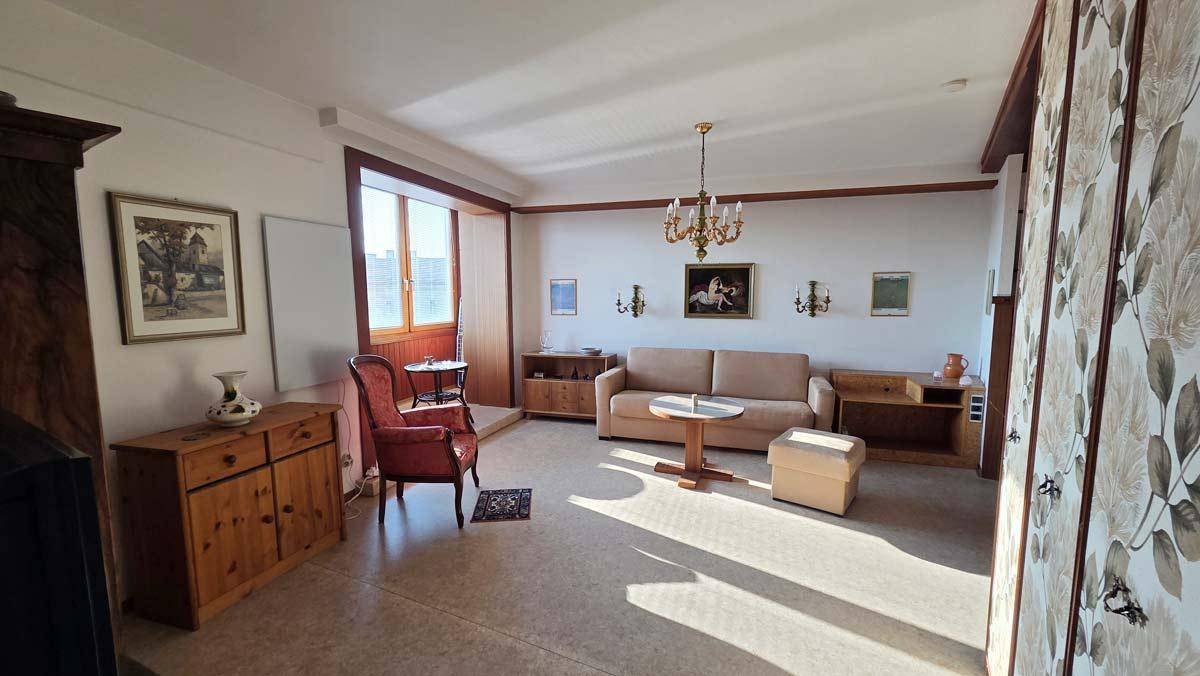 Helles Wohnzimmer mit gemütlicher Sitzecke, Teppichboden und traditioneller Einrichtung.