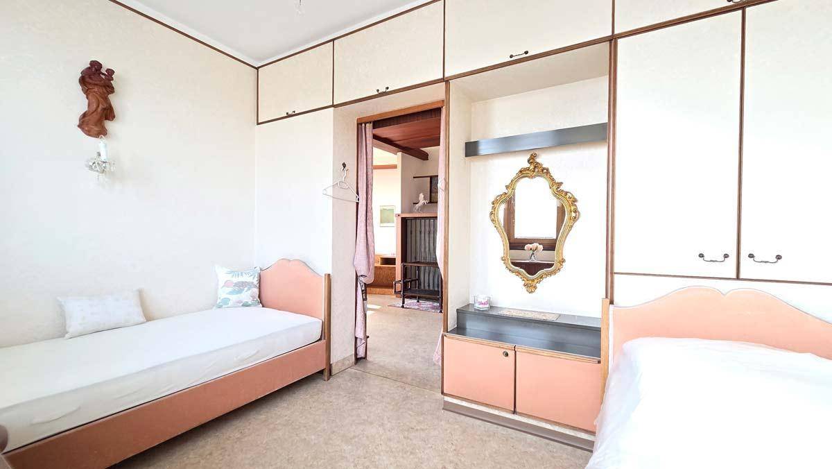 Schlafzimmer mit zwei Einzelbetten, Einbauschränken und traditionellem Spiegel.