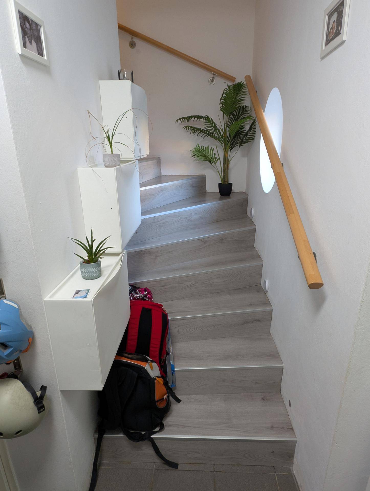 Helle Treppe mit Holzstufen und Holzgeländer, geschmückt mit Pflanzen, führt in die obere Etage.