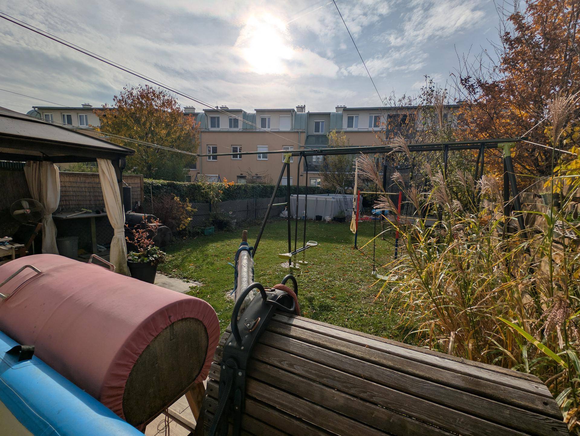 Weitläufiger Gartenbereich mit Rasen, Schaukel und Blick auf die umliegenden Reihenhäuser unter hellem Himmel.