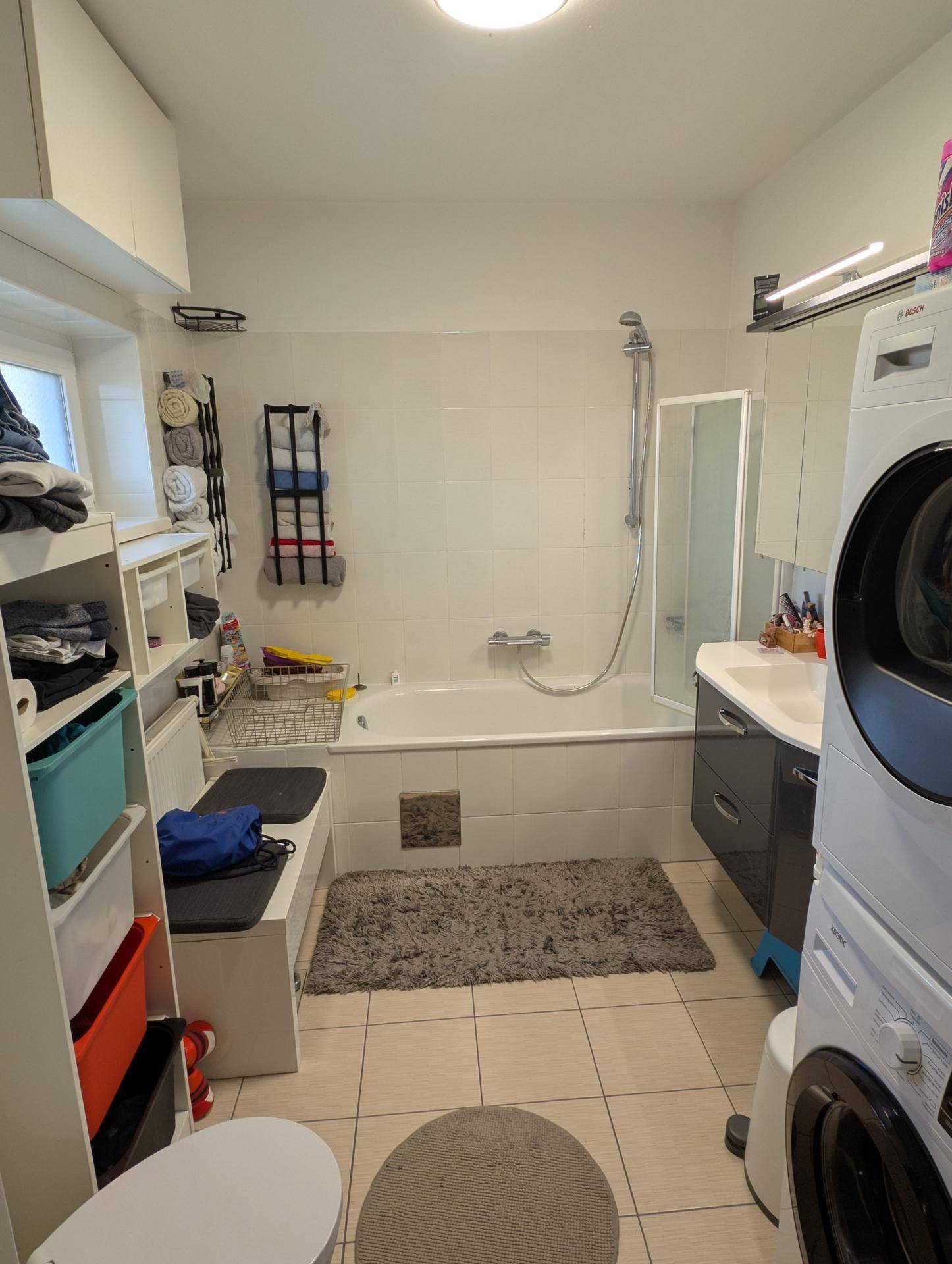 Funktionales Badezimmer mit Badewanne, Duschbereich, Waschbecken und integrierter Waschmaschine.