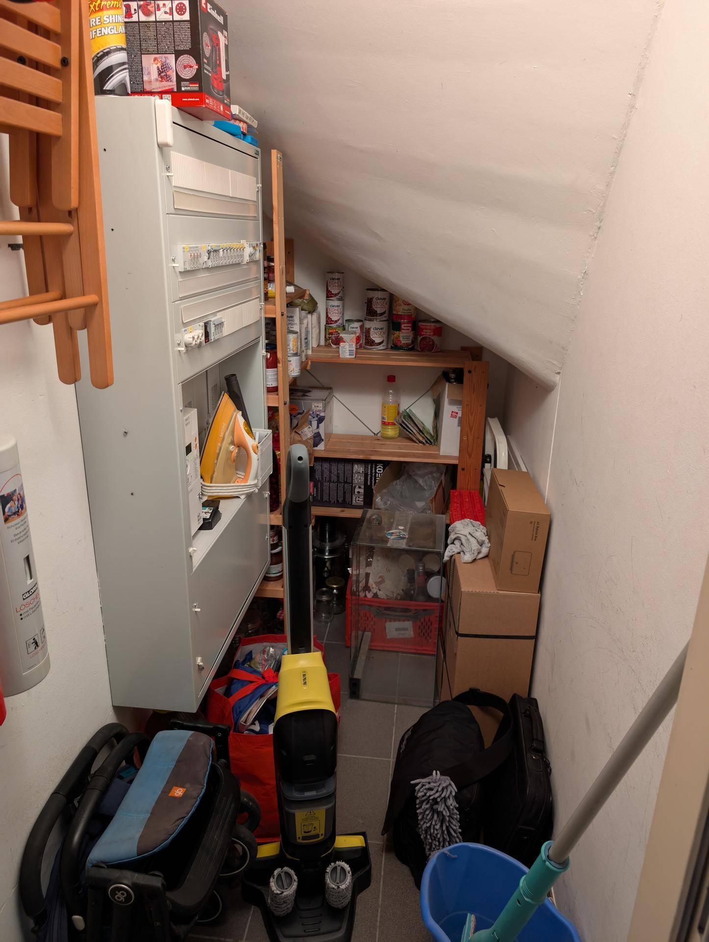 Praktischer Abstellraum unter einer Dachschräge mit Regalen und Platz für Haushaltsgeräte und Vorräte.