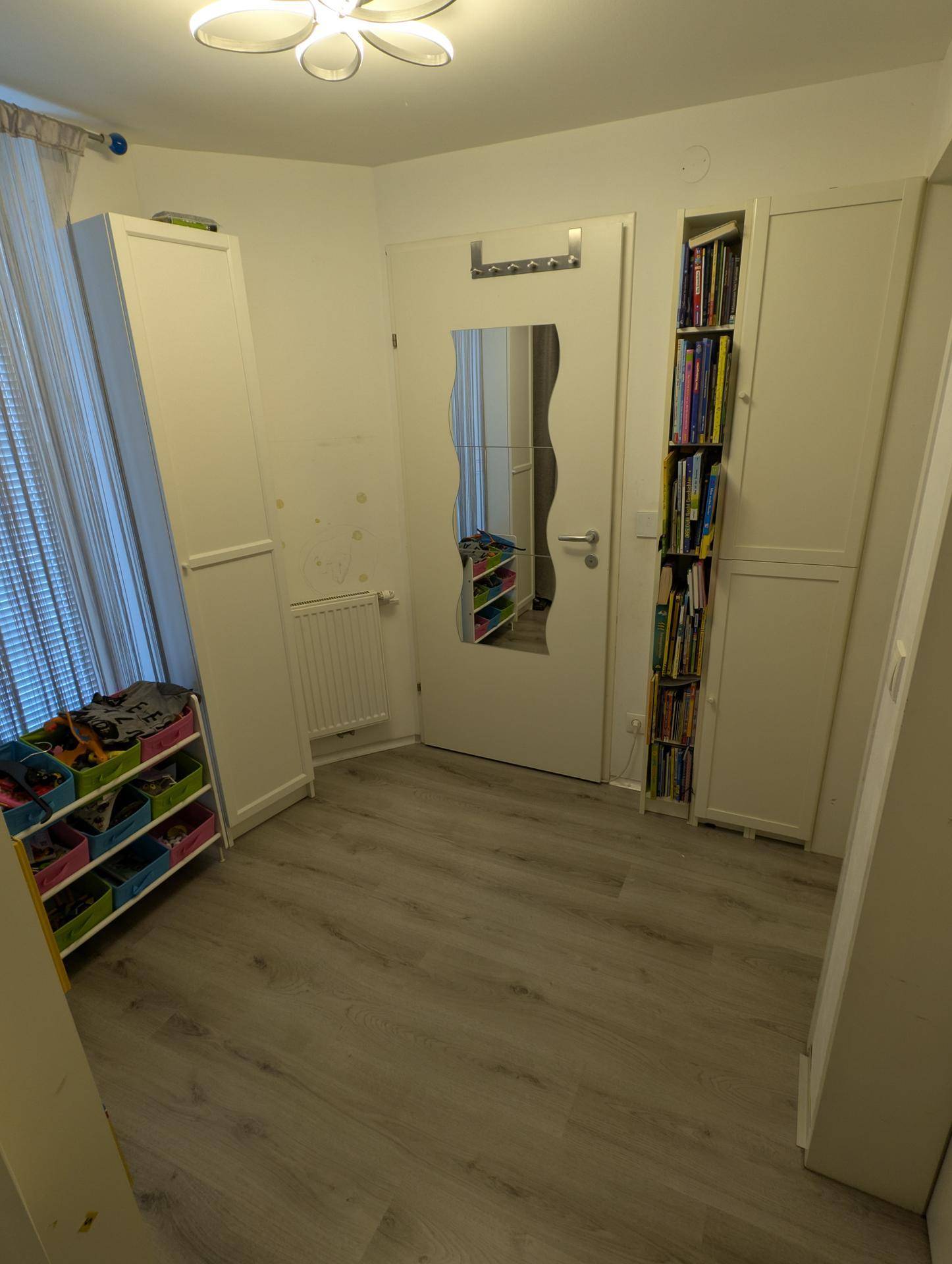 Raum mit hellem Laminatboden, Spiegeltür und integrierten Regalen, bietet zusätzlichen Stauraum.