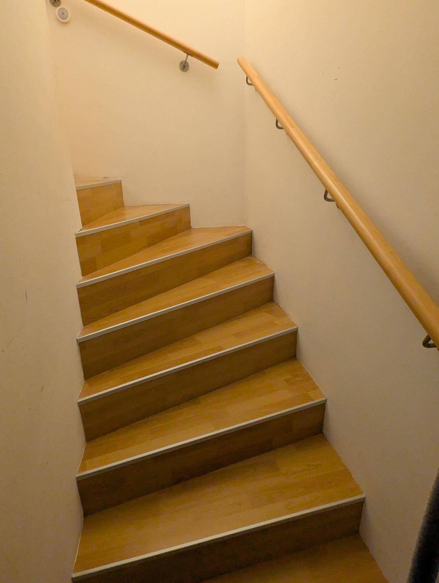 Helle Holztreppe mit Geländer, die zu den oberen Etagen des Hauses führt.
