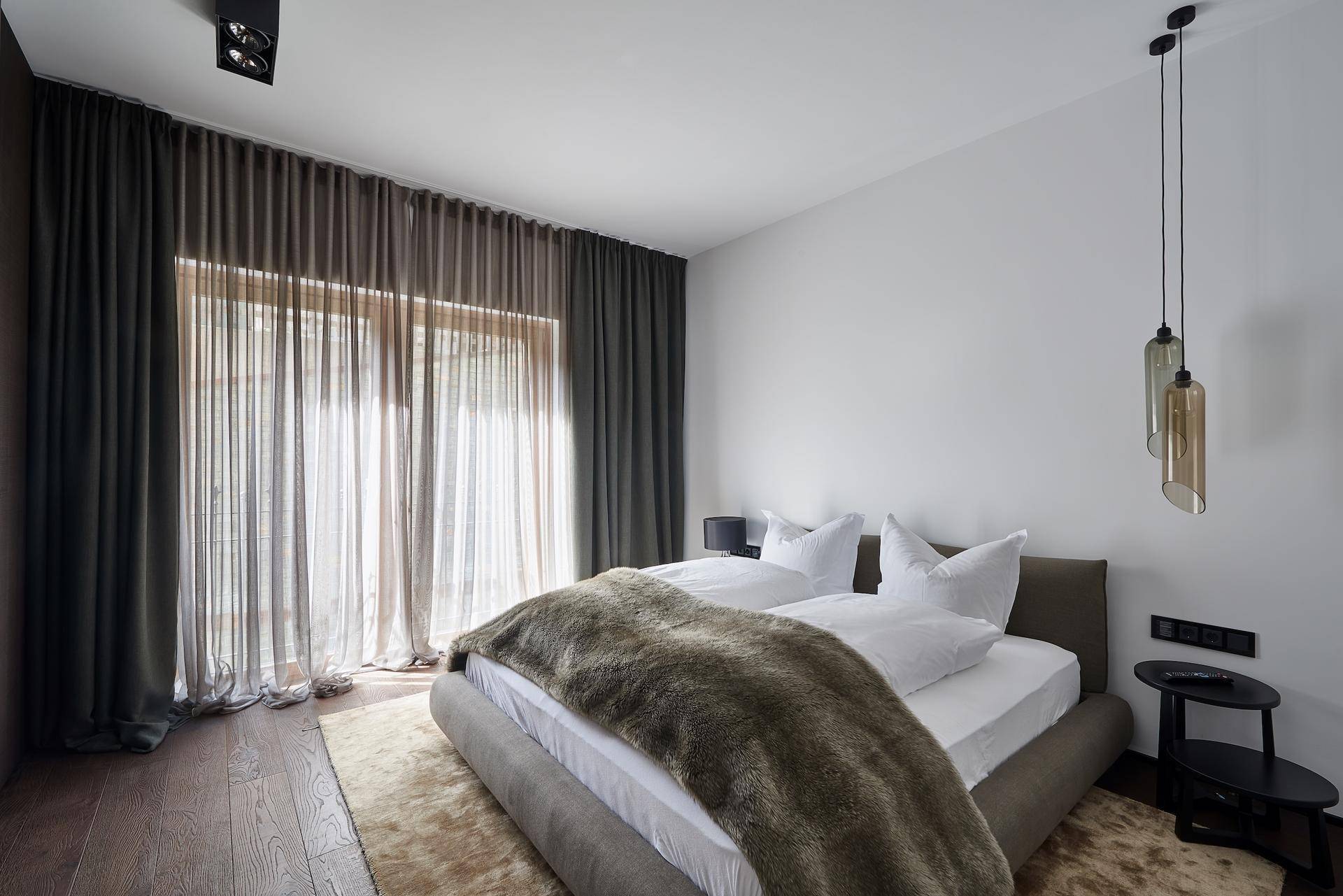 Gemütliches Schlafzimmer mit dunklen Vorhängen, Holzboden und viel natürlichem Licht.