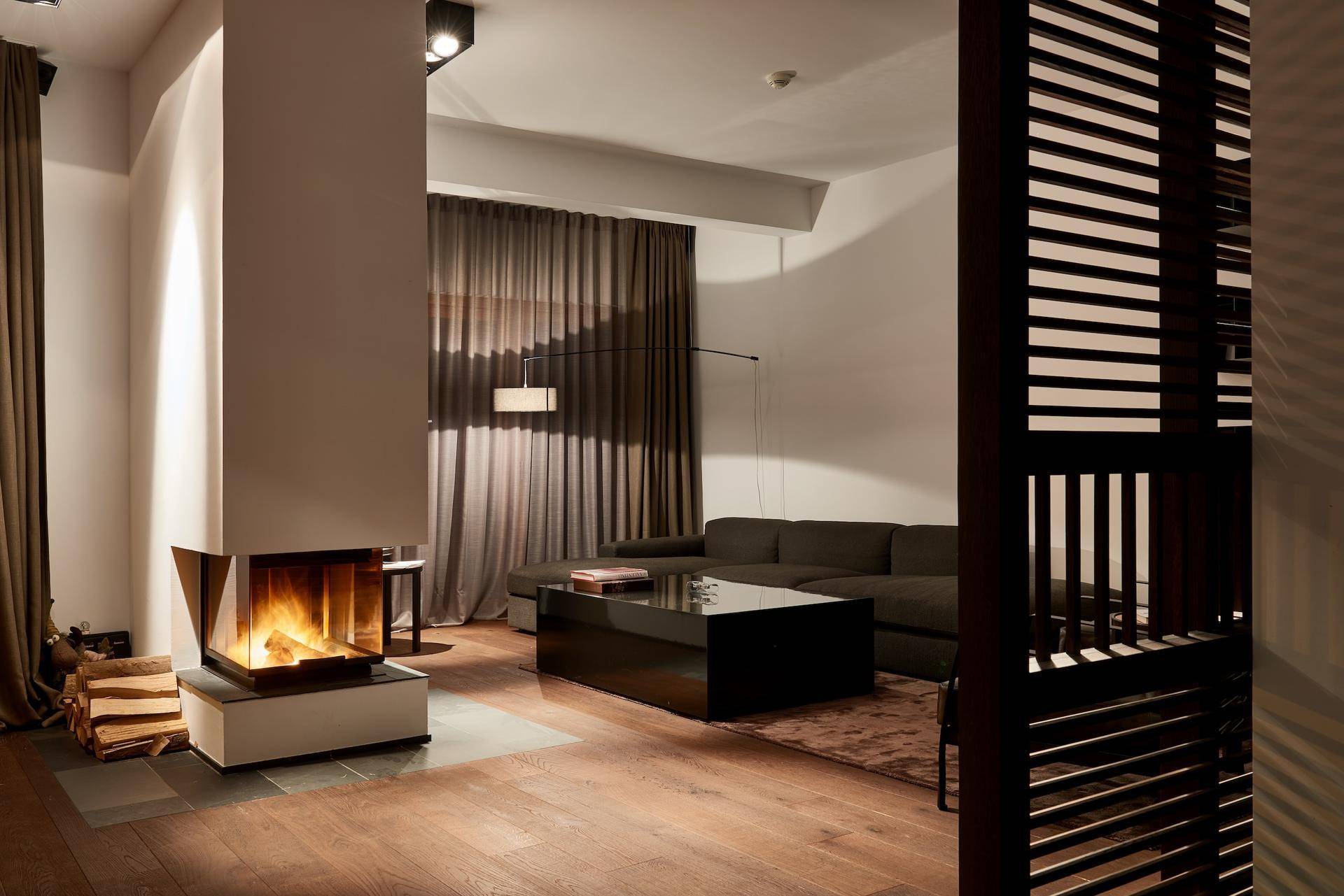 Gemütliches Wohnzimmer mit modernem Kamin, dunklem Sofa und Holzboden.