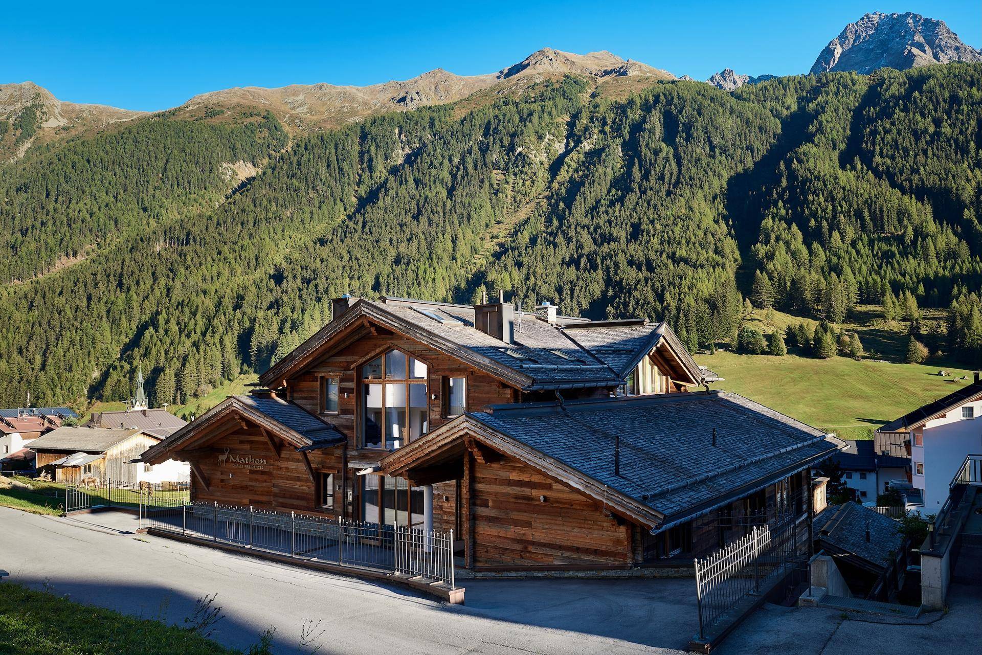 Beeindruckendes Chalet in alpiner Landschaft mit bewaldeten Bergen und grünen Wiesen.