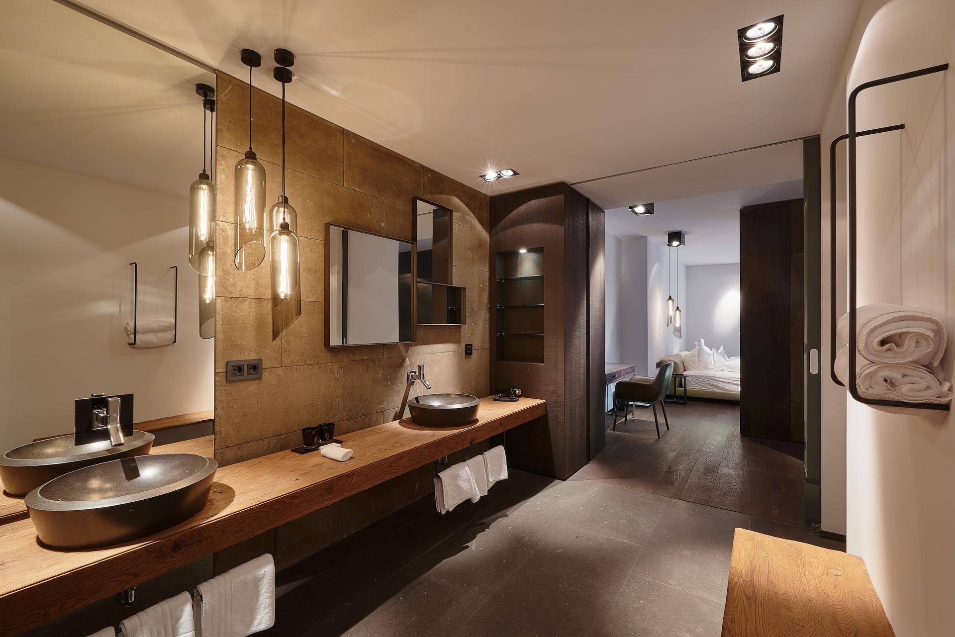 Luxuriöses Badezimmer mit Doppelwaschbecken, Steinwänden und Zugang zum Schlafbereich.