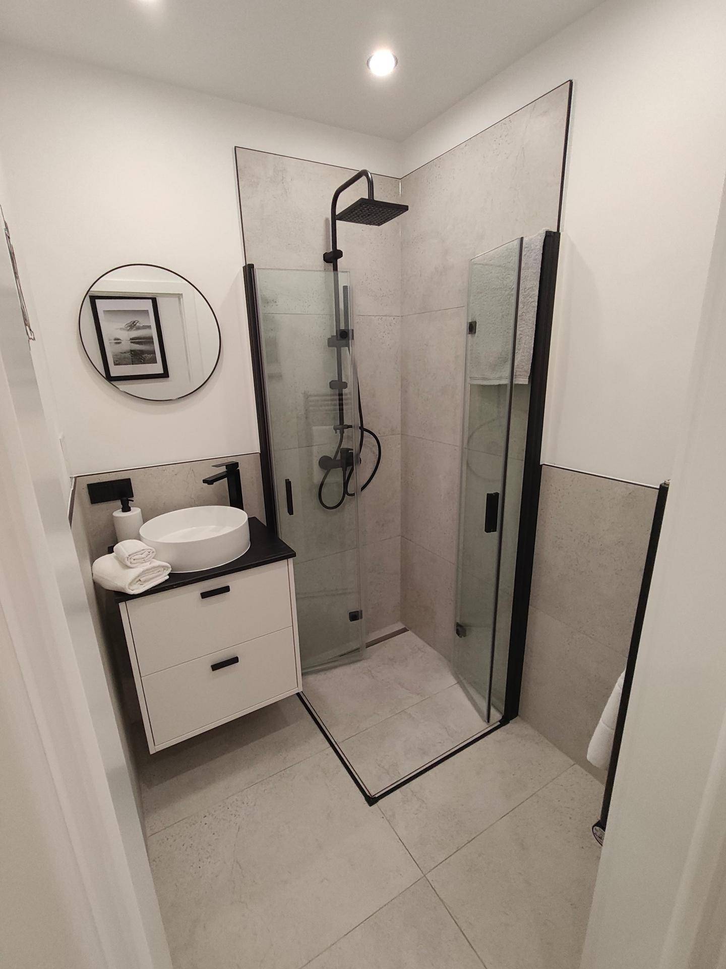 Elegantes Badezimmer mit moderner Eckdusche, Glasabtrennung und minimalistischem Design.