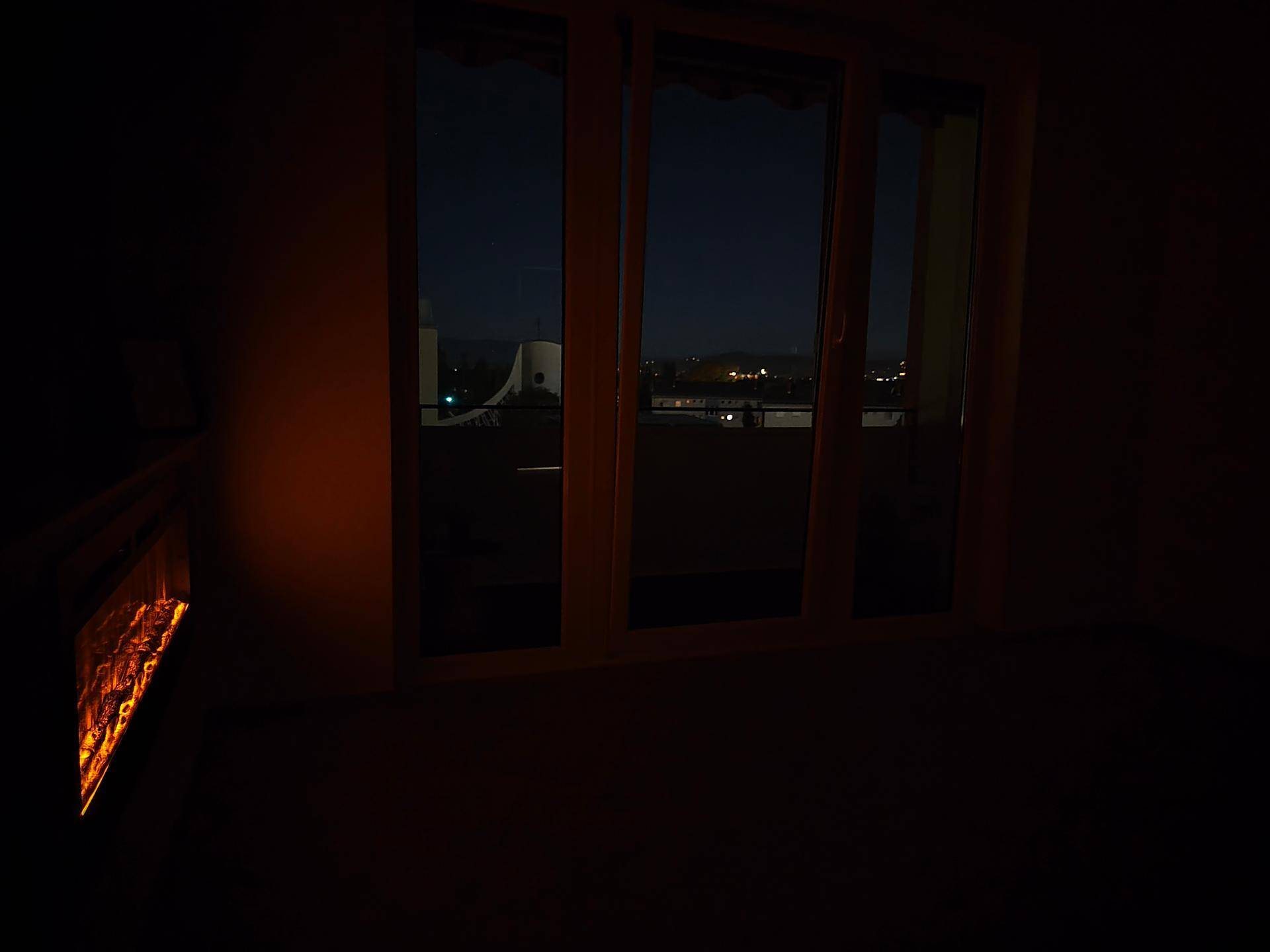 Dunkles Wohnzimmer bei Nacht mit beleuchtetem Elektrokamin und Blick nach draußen.