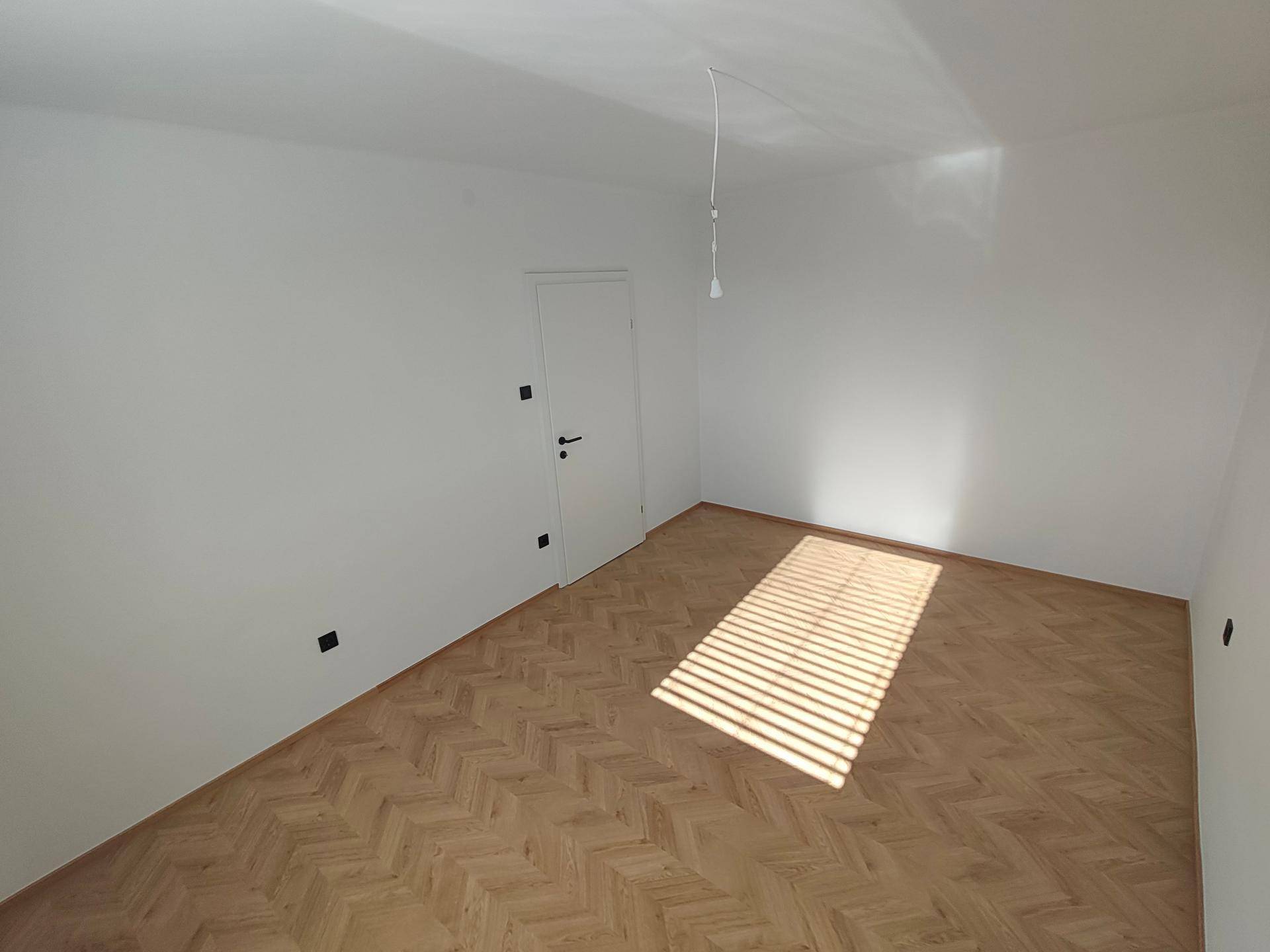 Geräumiges Zimmer mit Fischgrätparkett und sonnigem Lichteinfall durch das Fenster.