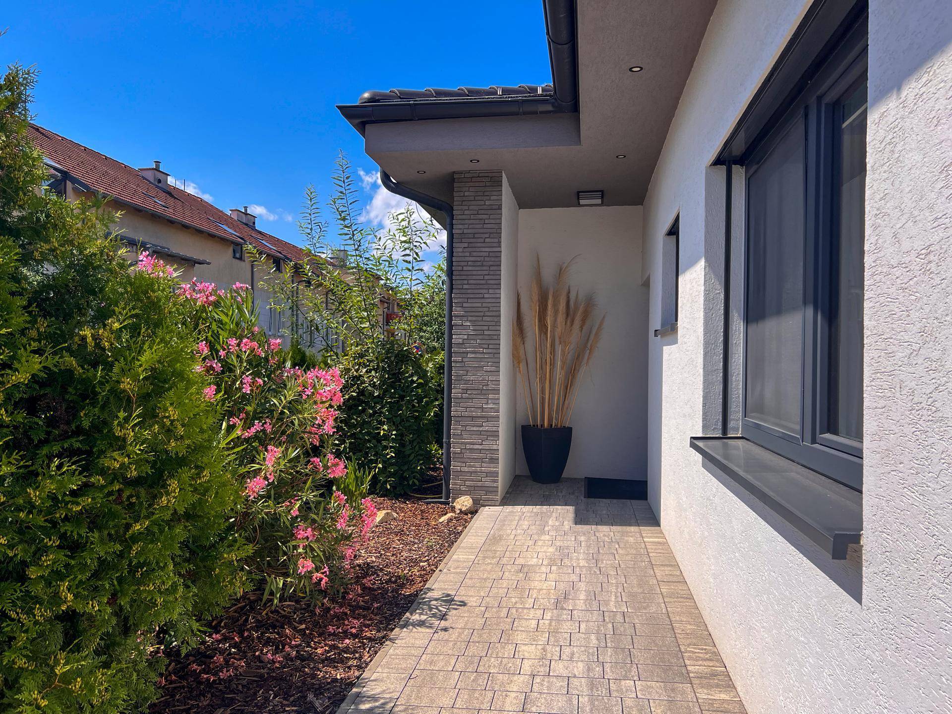 Eingangsbereich des Hauses mit gepflastertem Weg und grüner Bepflanzung.