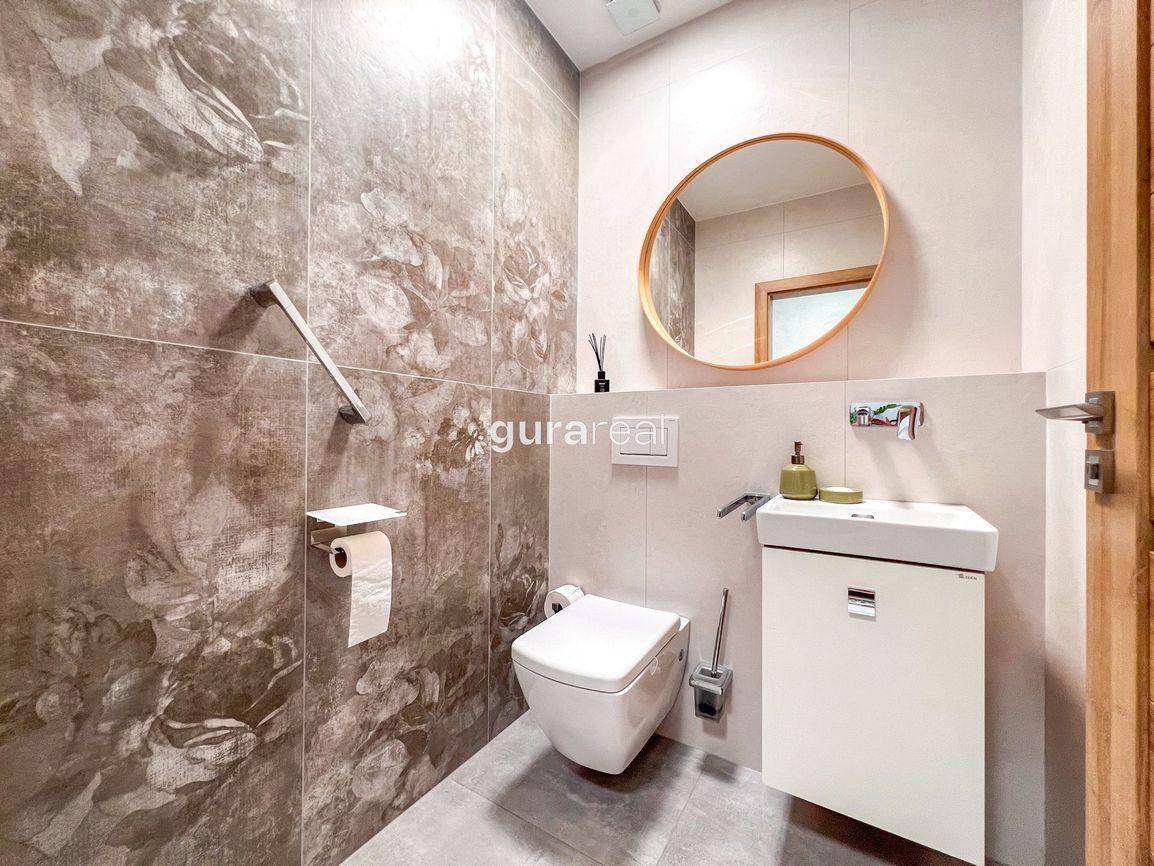 Modernes Gäste-WC mit Wand-WC, kleinem Waschbecken und rundem Spiegel.