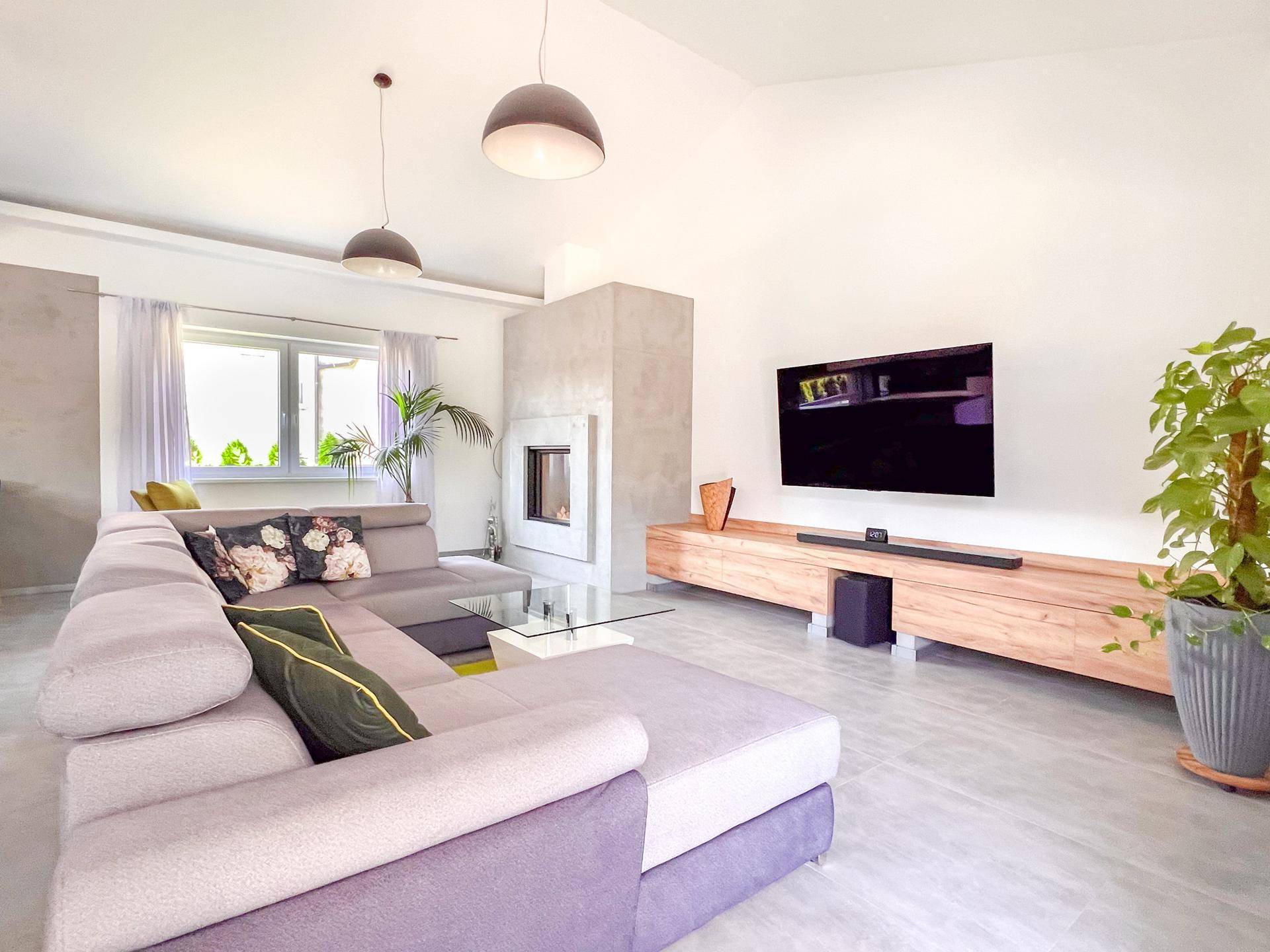 Helles Wohnzimmer mit großer Eckcouch, Kamin und Wandfernseher.