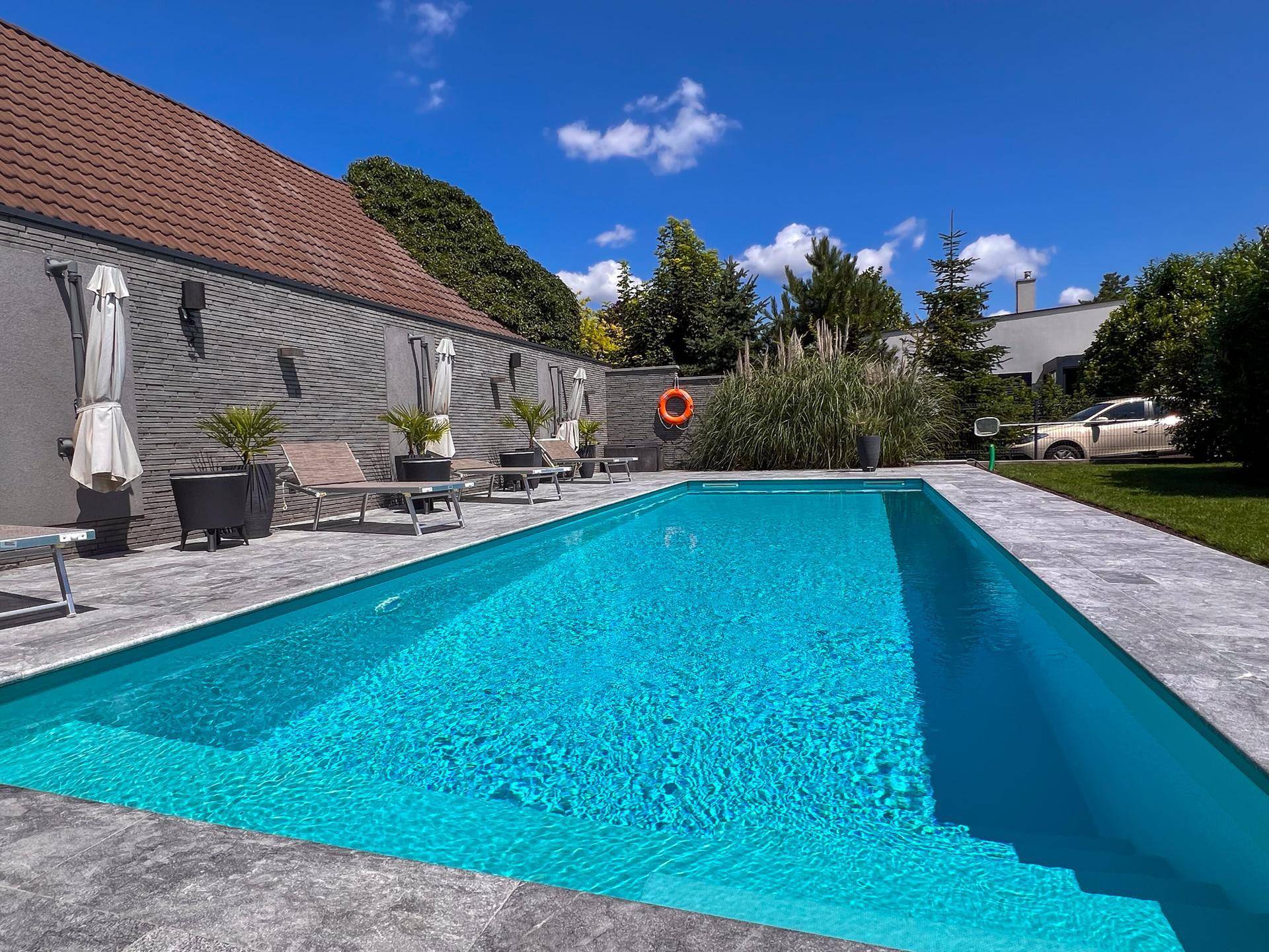 Langer, sauberer Swimmingpool im Gartenbereich mit blauer Fliesenverkleidung.