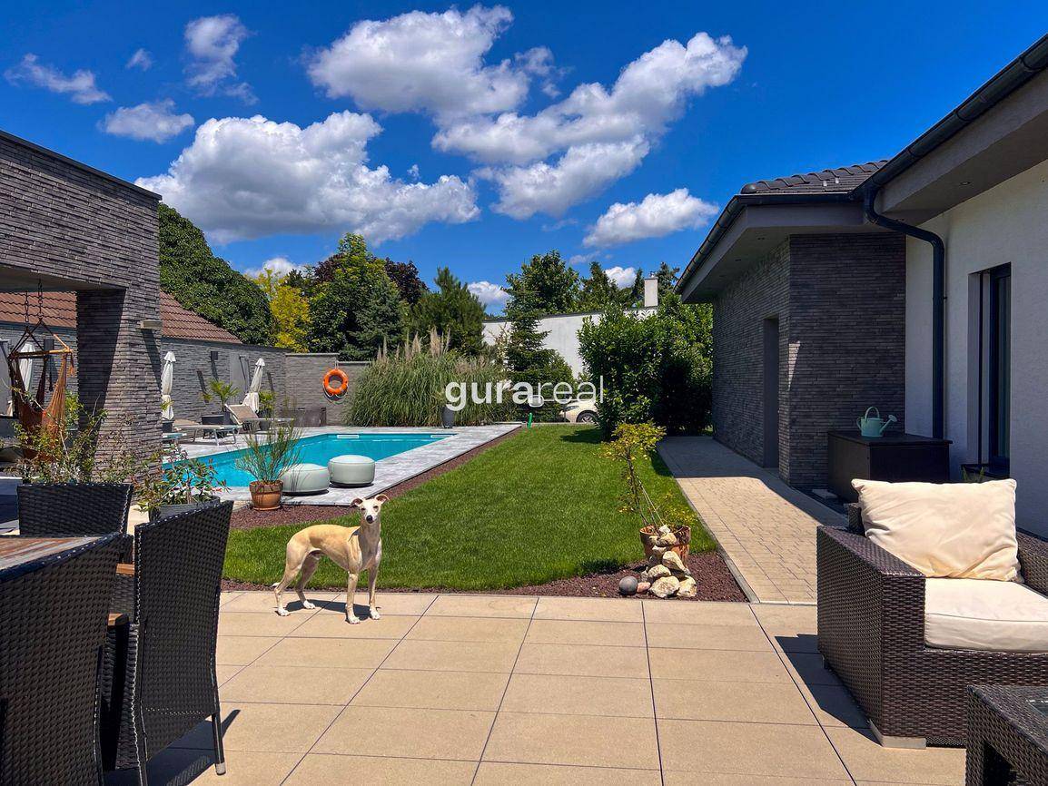 Geräumiger Garten mit Terrasse, Sitzbereich und Blick auf den Pool unter blauem Himmel.